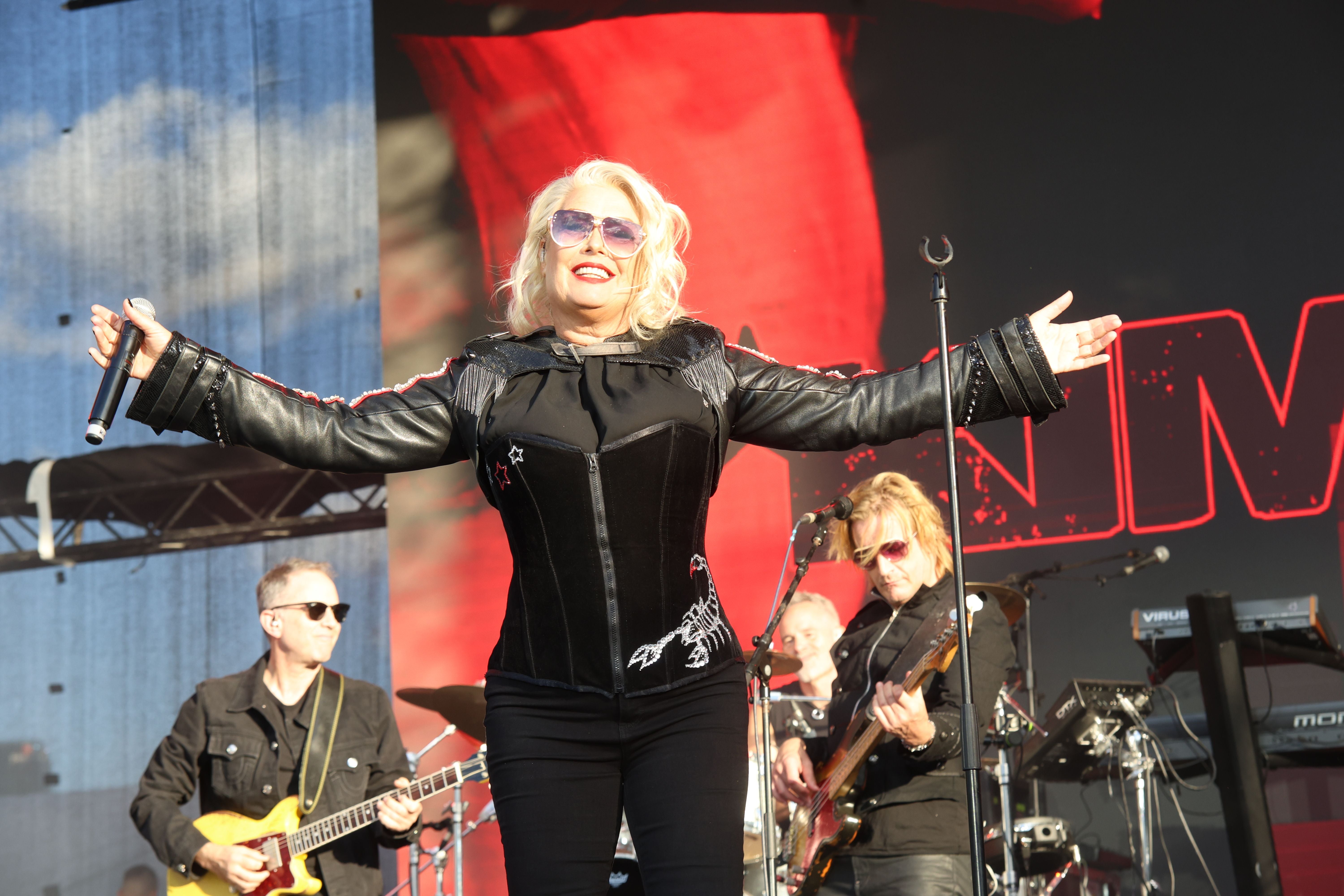 Kim Wilde singt auf einer Bühne mit Band im Hintergrund bei einem Open-Air-Konzert.