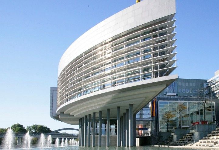 Modernes Bürogebäude auf Pfeilern mit Wasserbecken und Fontänen im Vordergrund.