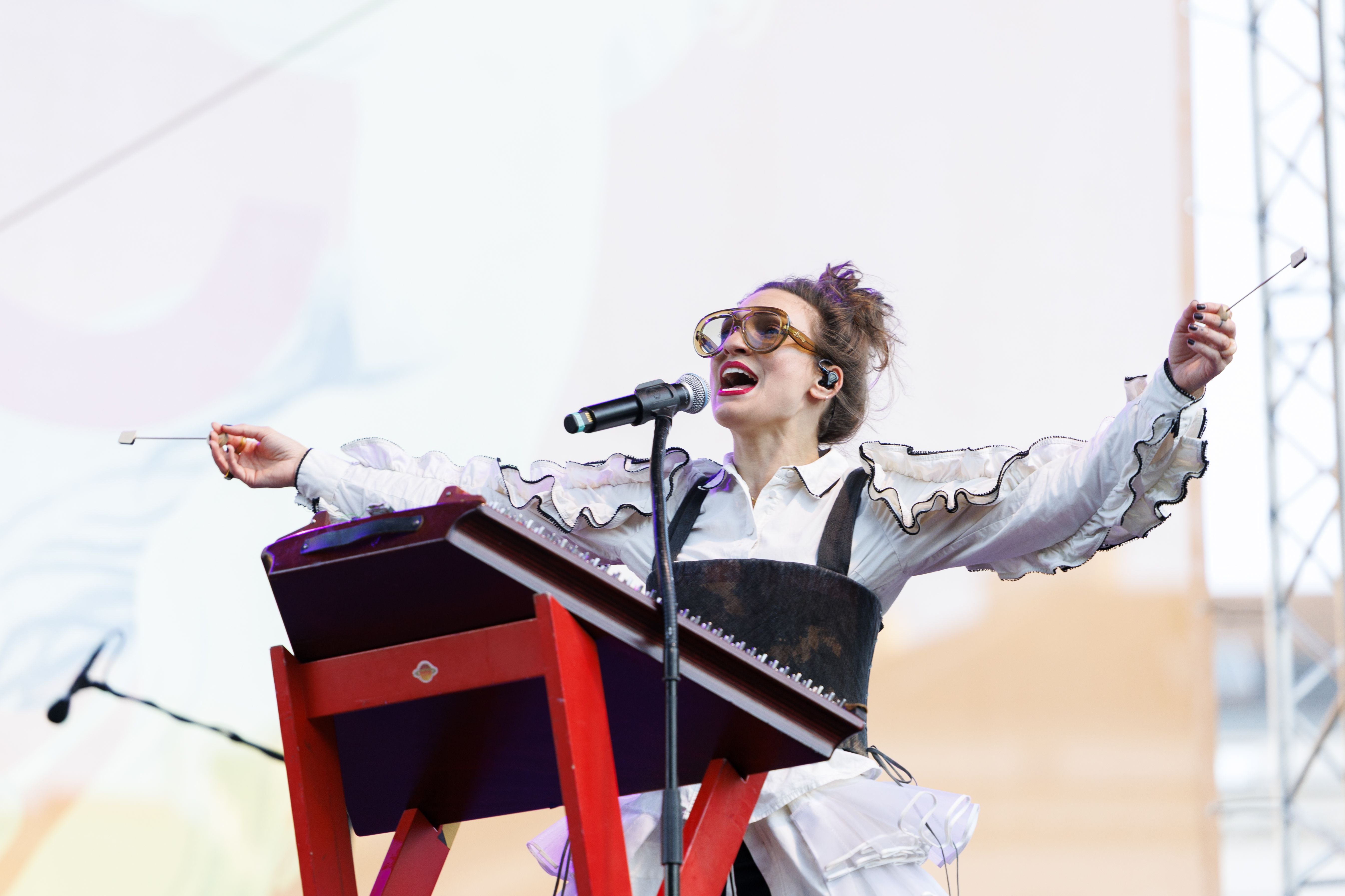 Musikerin spielt auf der Bühne mit ausgebreiteten Armen und singt ins Mikrofon.