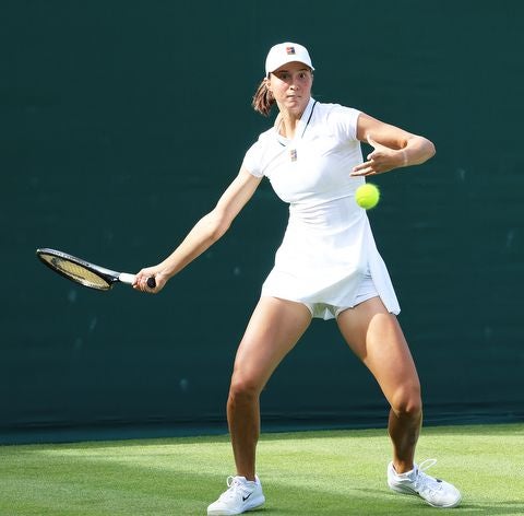 Tennisspielerin in weißem Outfit schlägt einen Ball auf einem Rasenplatz.