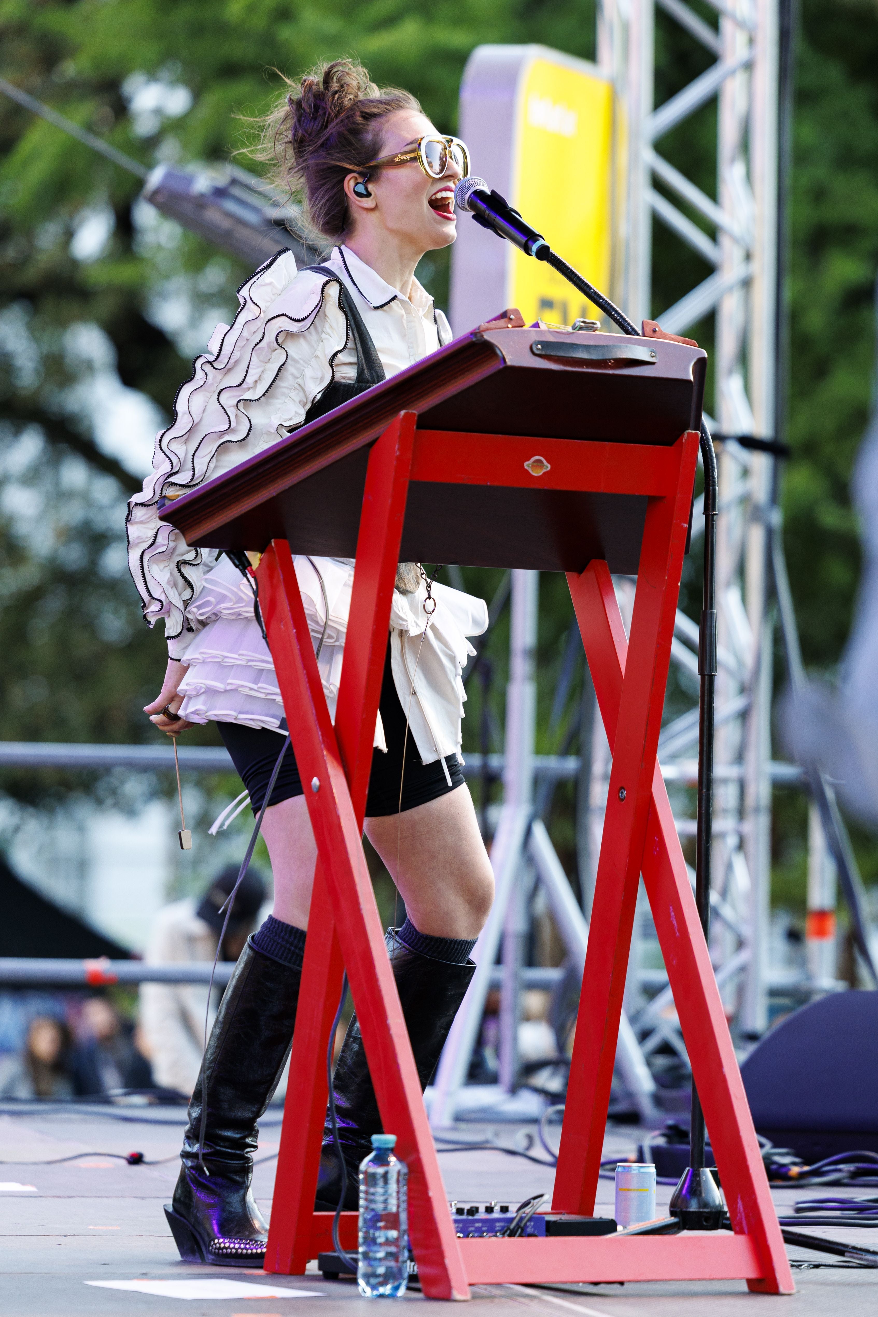 Frau in auffälligem Outfit singt auf einer Bühne hinter einem roten Keyboard.