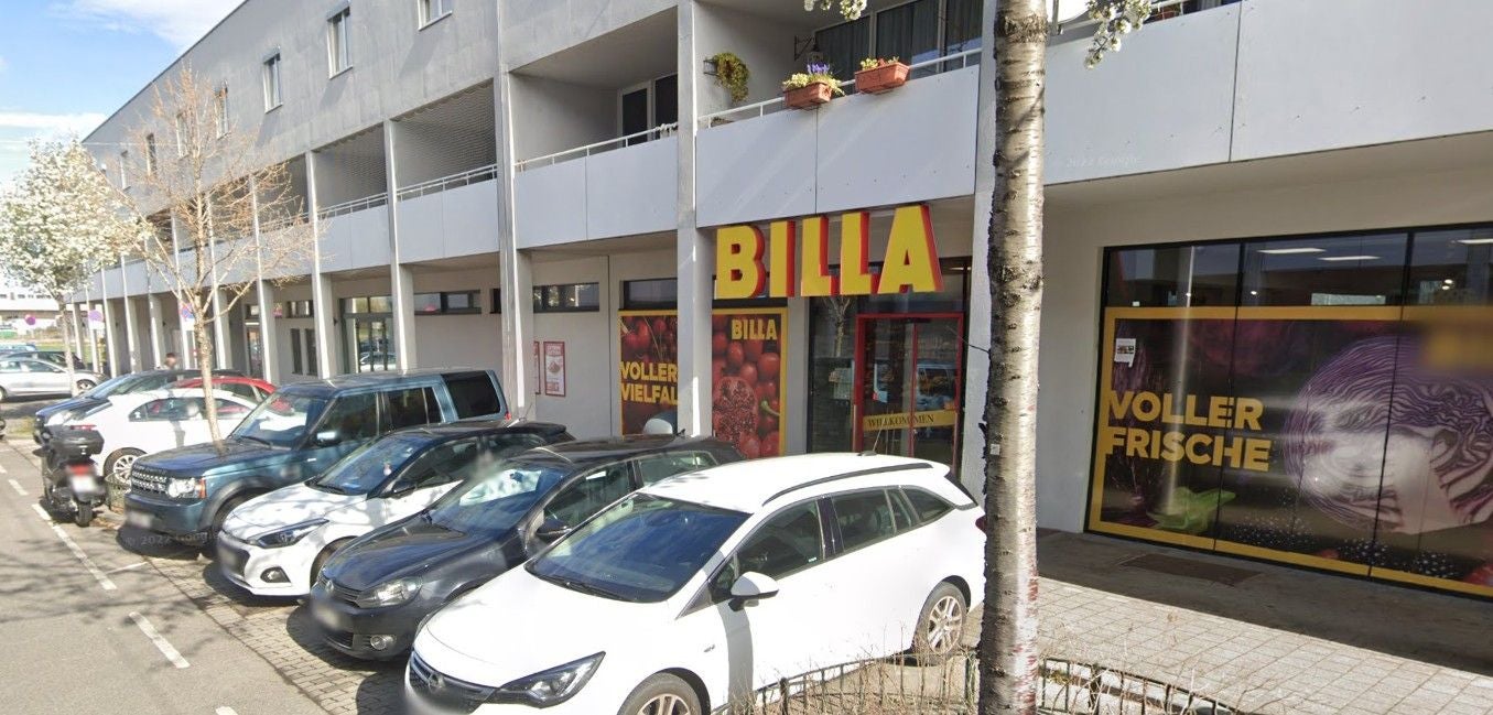 Eingang eines BILLA-Supermarkts mit parkenden Autos davor in der Eibengasse 57, Wien.