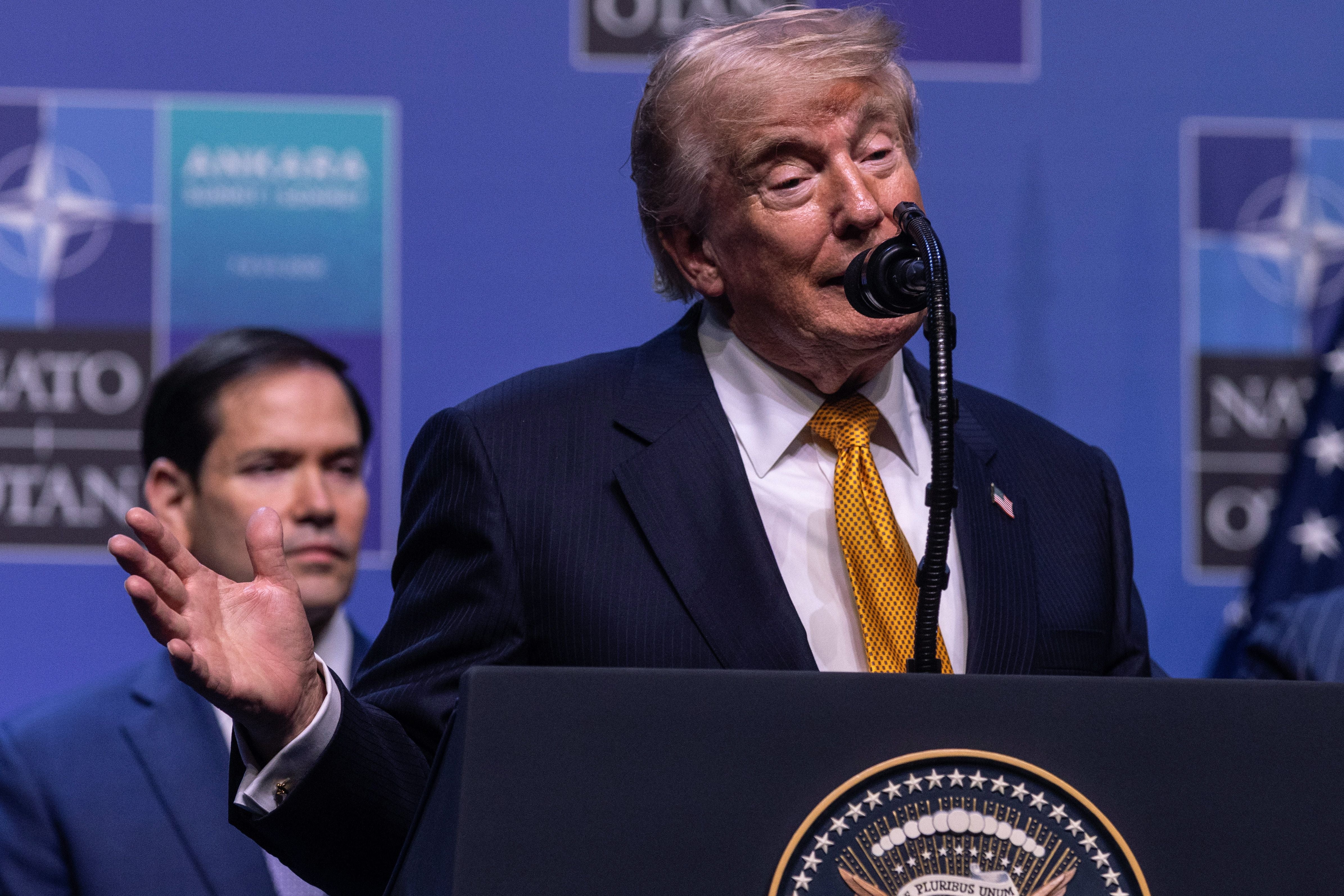 Ein Mann im Anzug spricht auf einer Pressekonferenz vor einem NATO-Logo und einem Mikrofon.