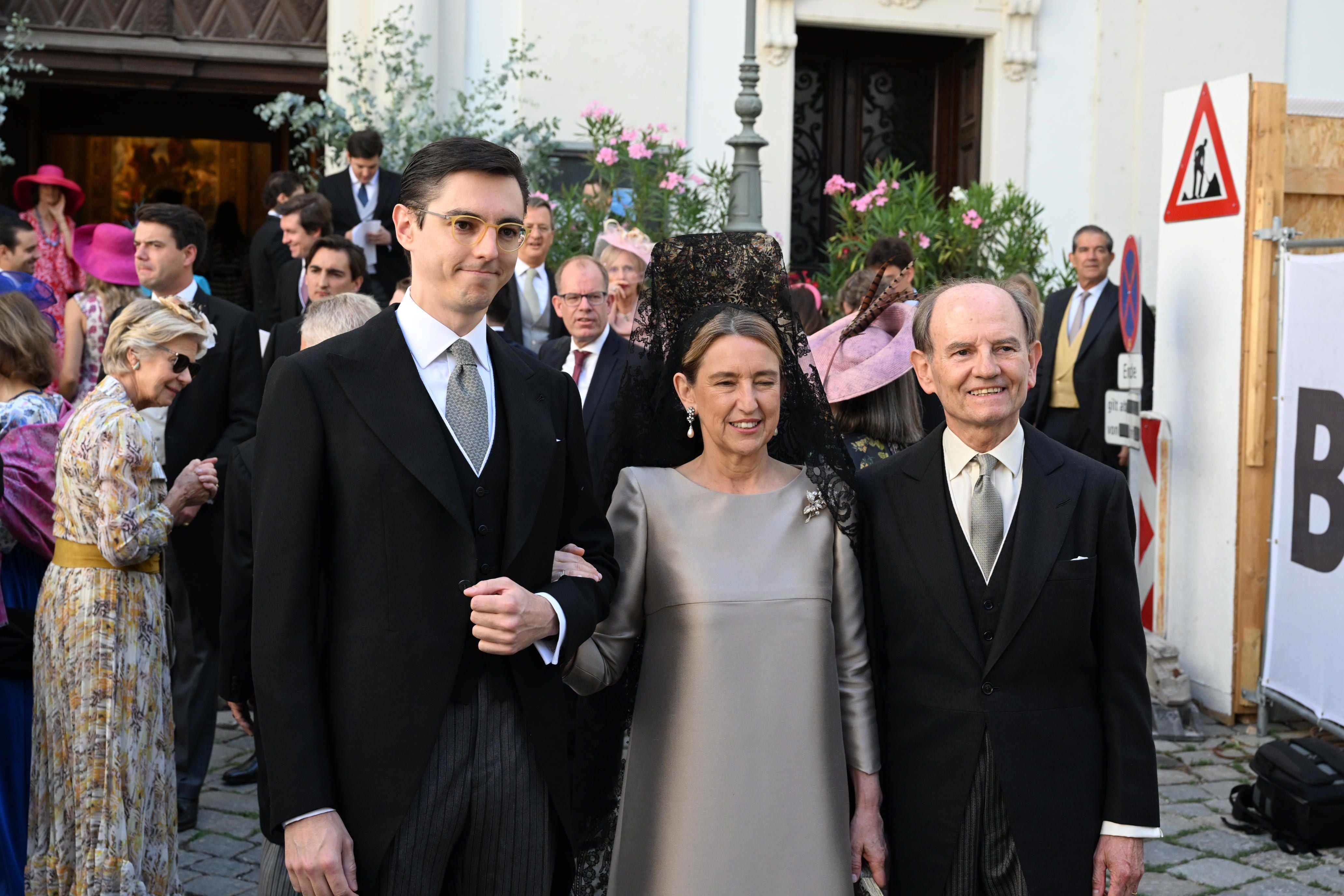Drei festlich gekleidete Personen posieren bei einer Hochzeit vor einer Kirche.