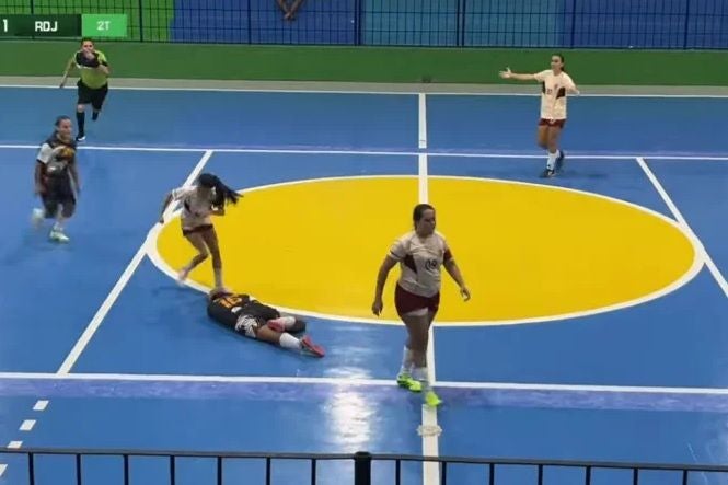 Futsal-Spielerinnen auf einem blauen Spielfeld, eine liegt am Boden, andere laufen weiter.