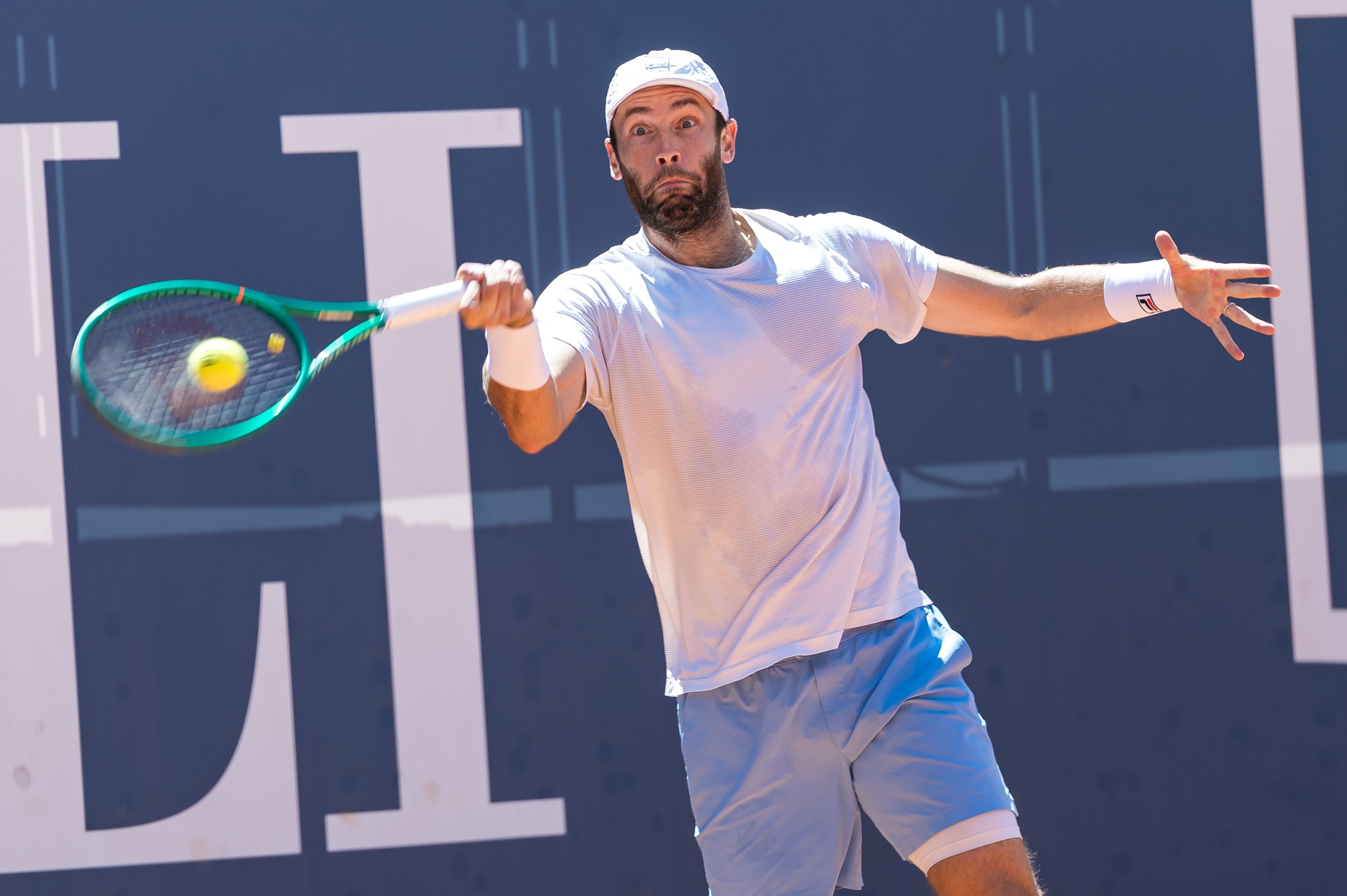 Ein Tennisspieler schlägt den Ball bei einem Match auf Sandplatz.