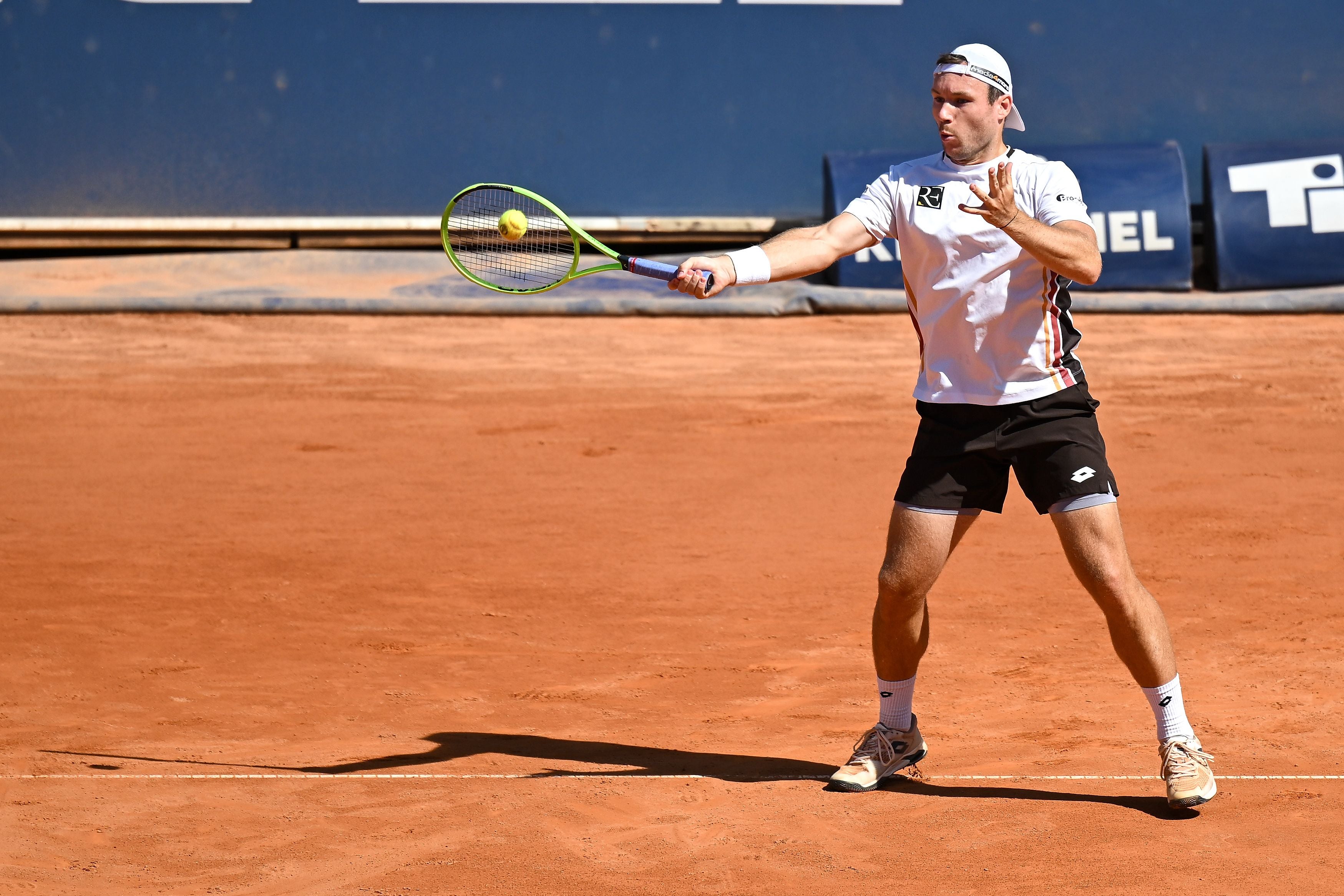 Ein Tennisspieler schlägt auf einem Sandplatz einen Ball mit einer Vorhand.