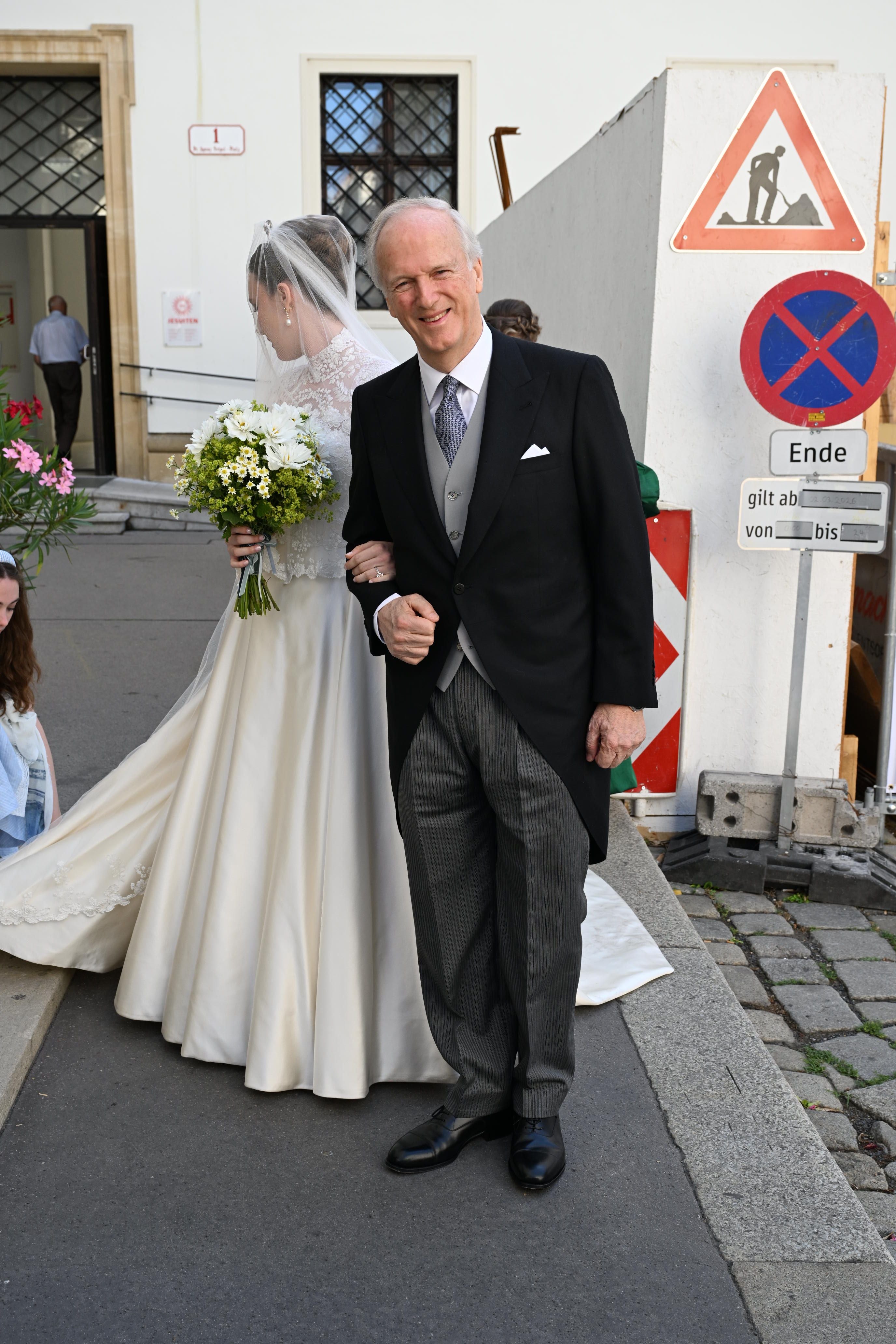 Ein Mann im Anzug und eine Braut im Hochzeitskleid stehen vor einer Baustelle.