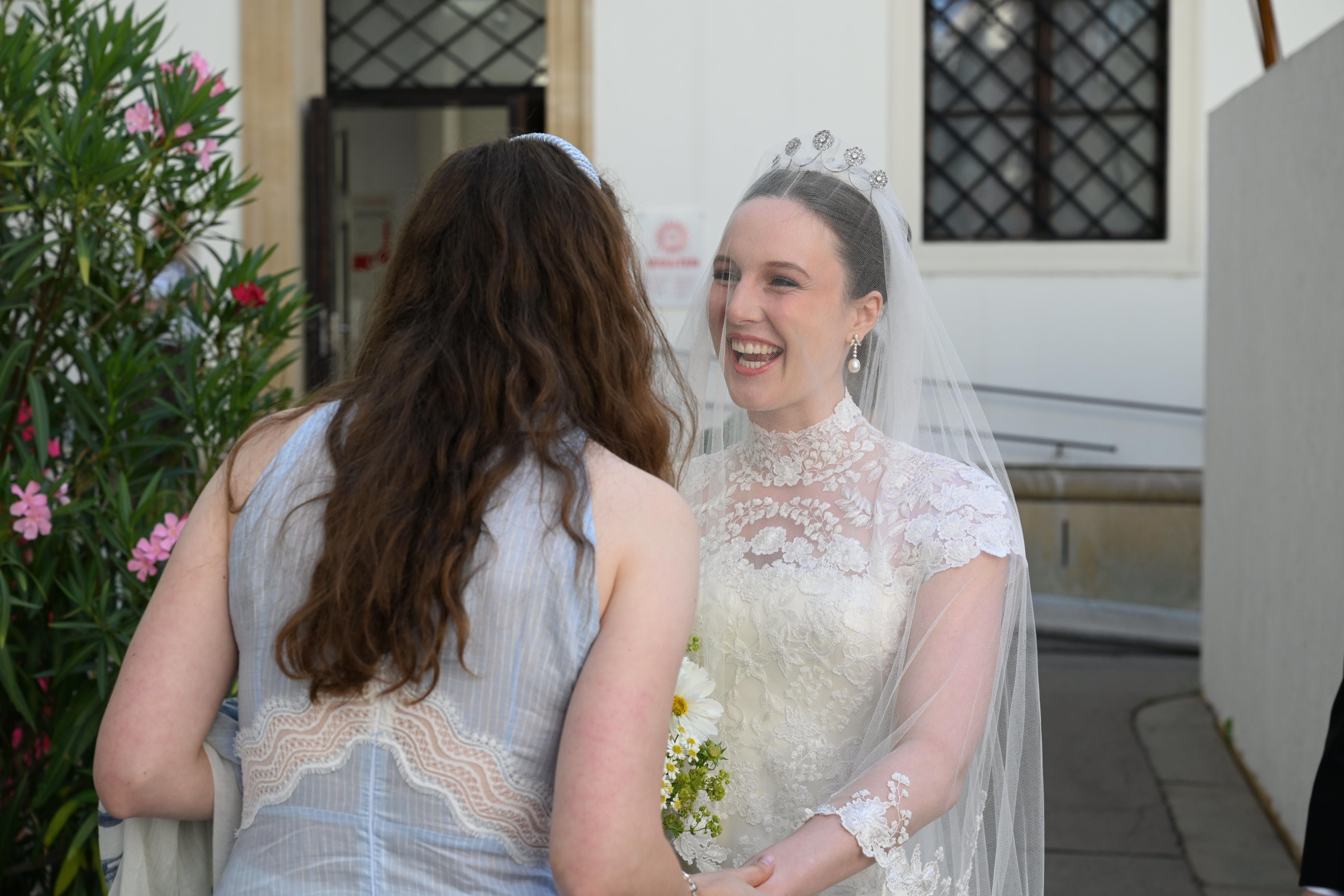 Eine Braut im Hochzeitskleid lächelt und hält die Hand einer Frau im Freien.