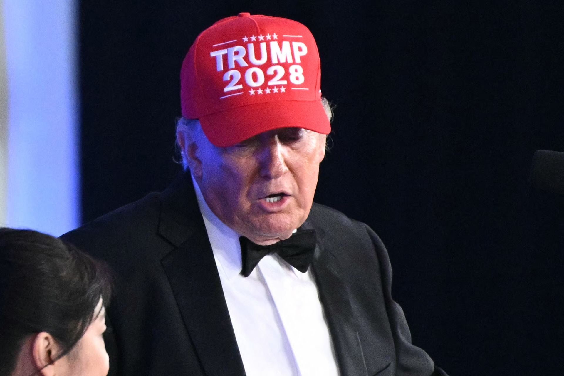 Ein Mann im Smoking trägt eine rote Kappe mit der Aufschrift "TRUMP 2028" und spricht.