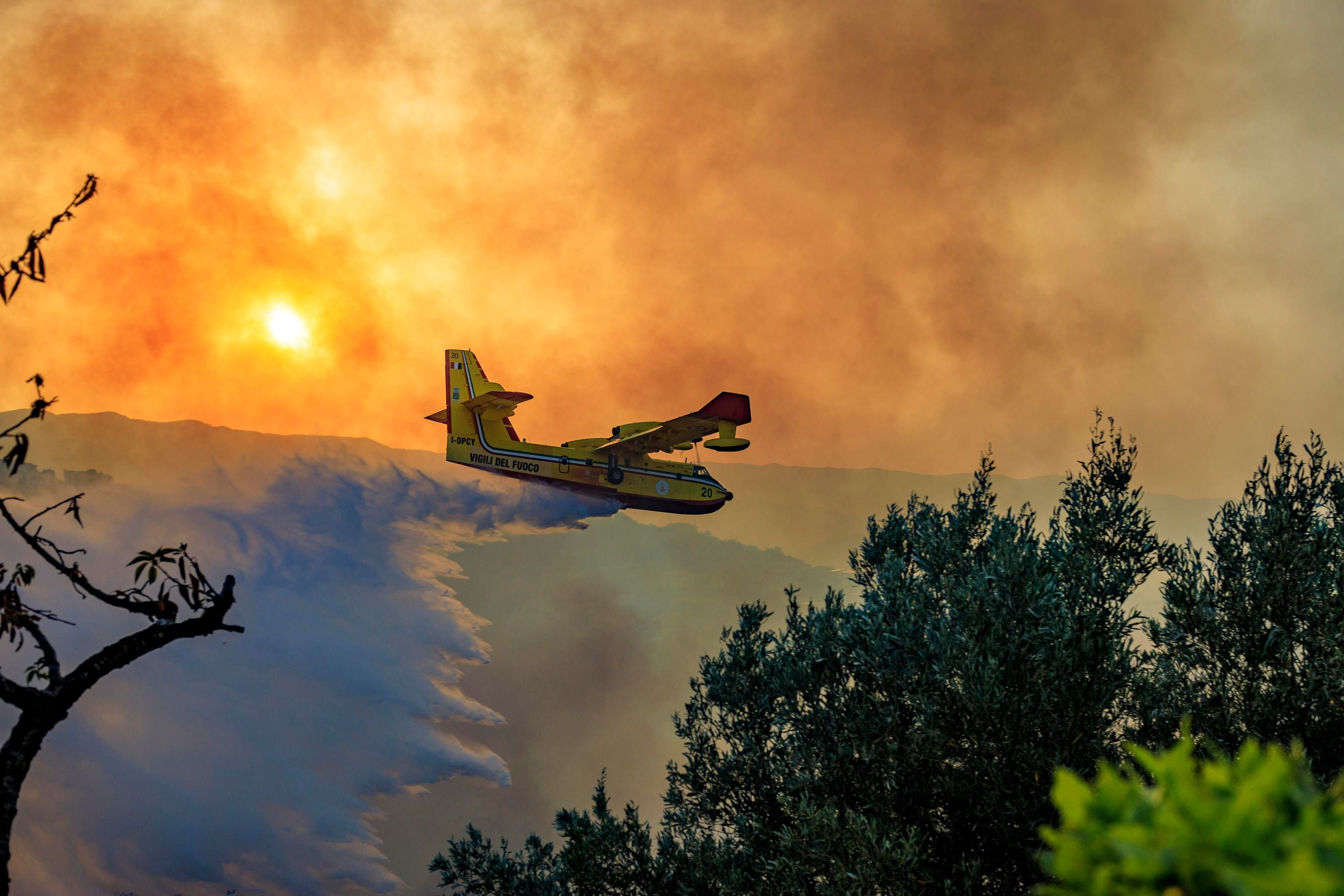 Löschflugzeug wirft Wasser über einen Waldbrand bei Sonnenuntergang in Italien ab.
