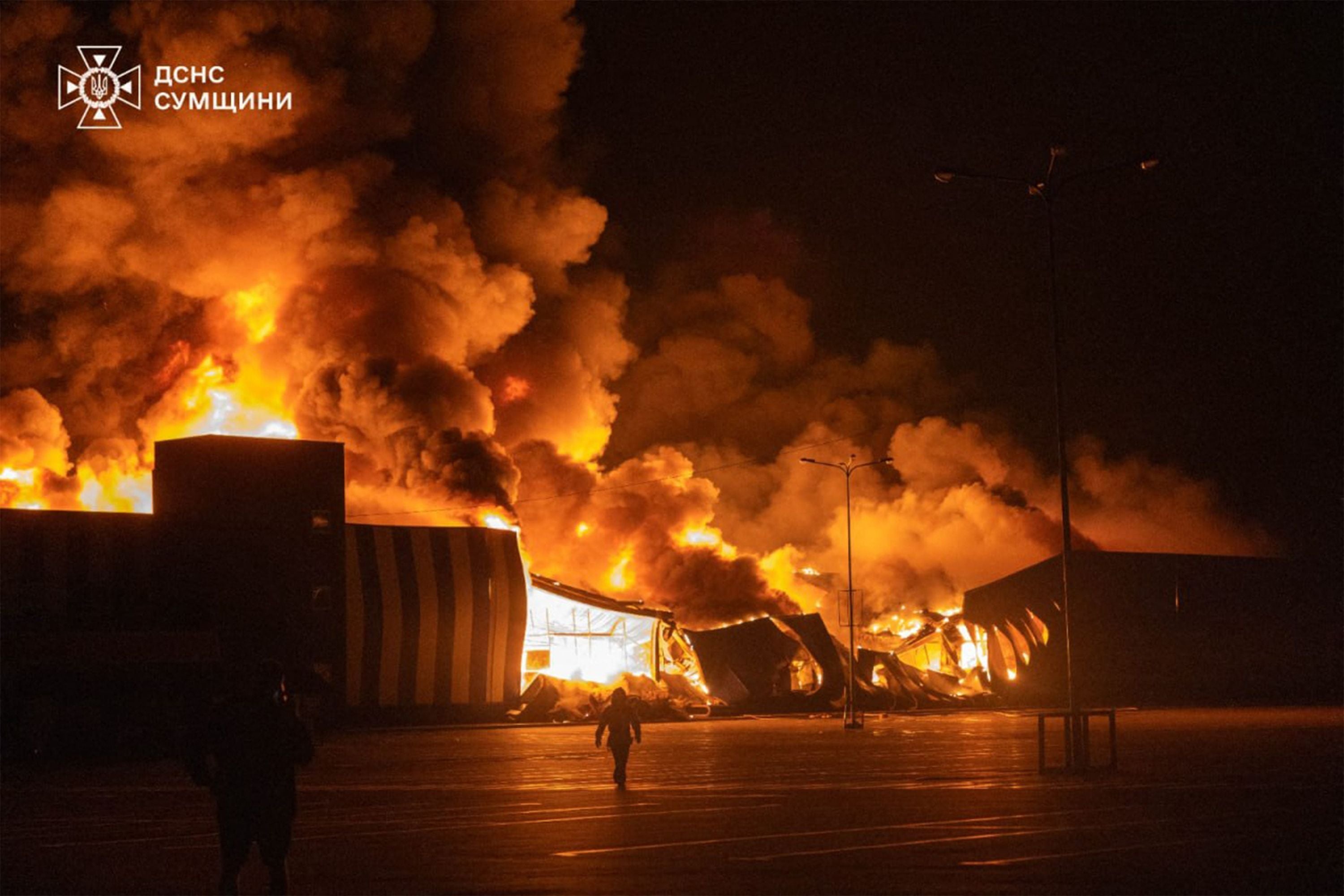 Großbrand in einem Einkaufszentrum bei Nacht, Feuerwehrleute bekämpfen das Feuer, dichter Rauch steigt auf.
