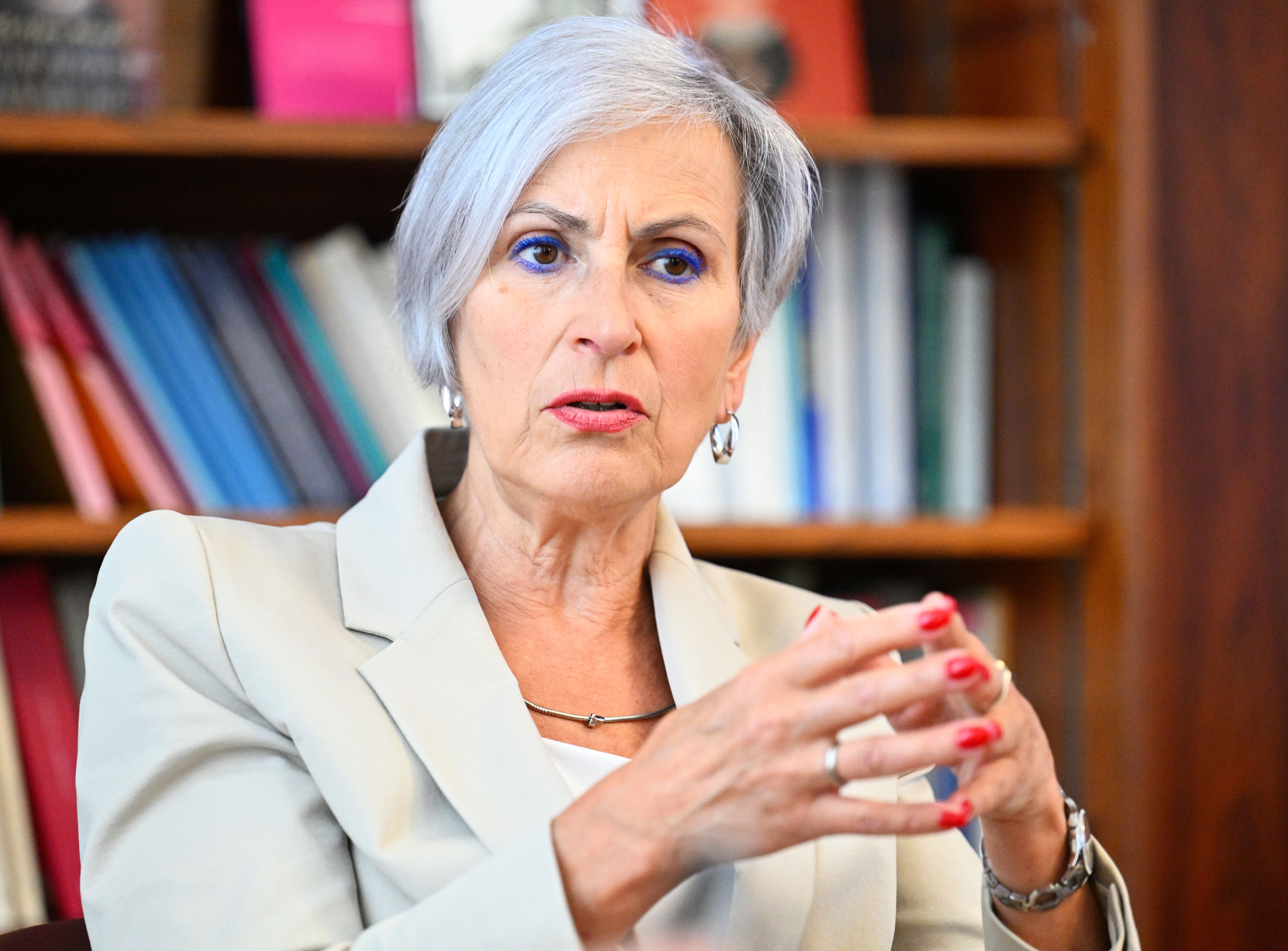 Ältere Frau mit grauem Haar spricht im Interview, Bücherregal im Hintergrund.