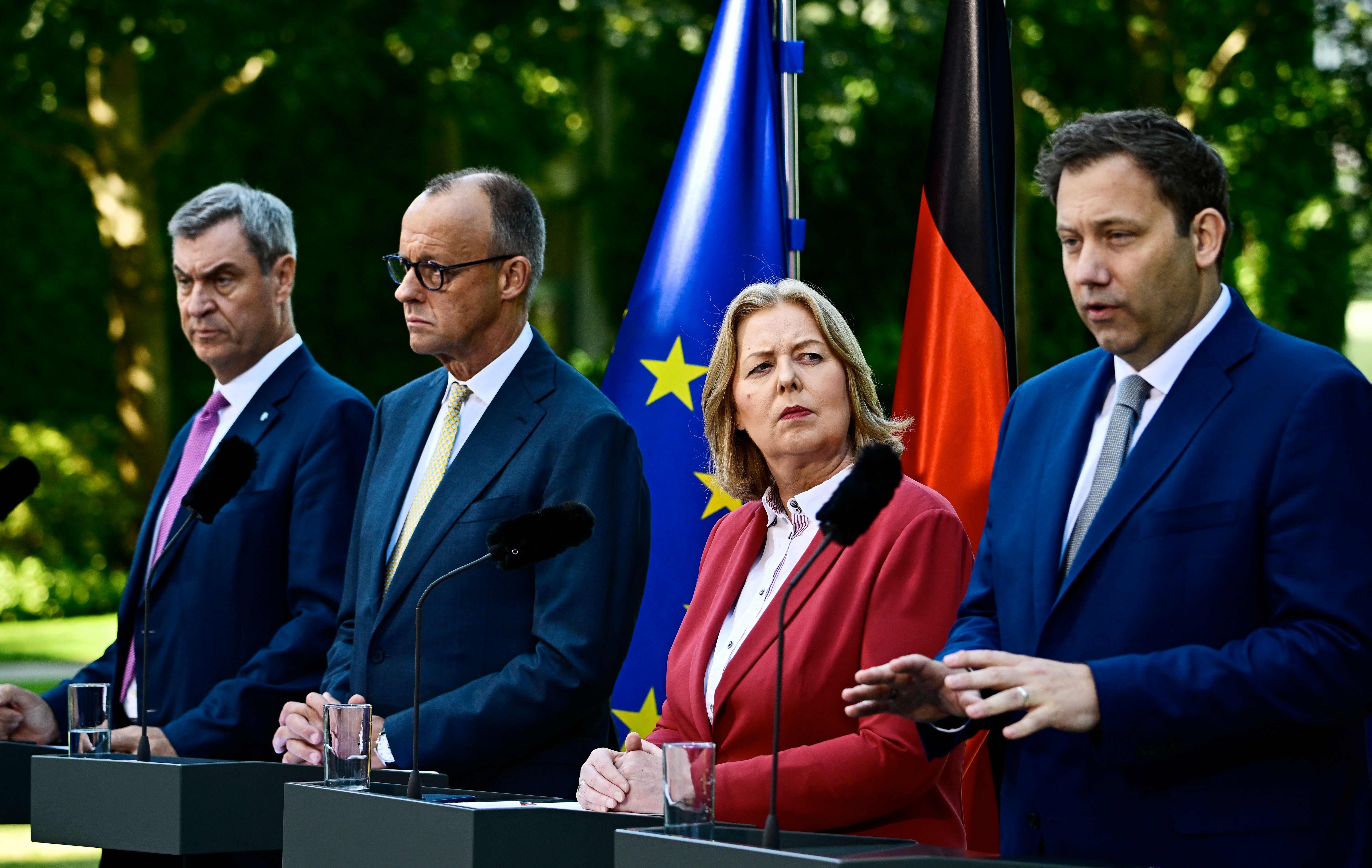 Vier Politiker stehen bei einer Pressekonferenz im Freien vor EU- und Deutschlandflaggen.