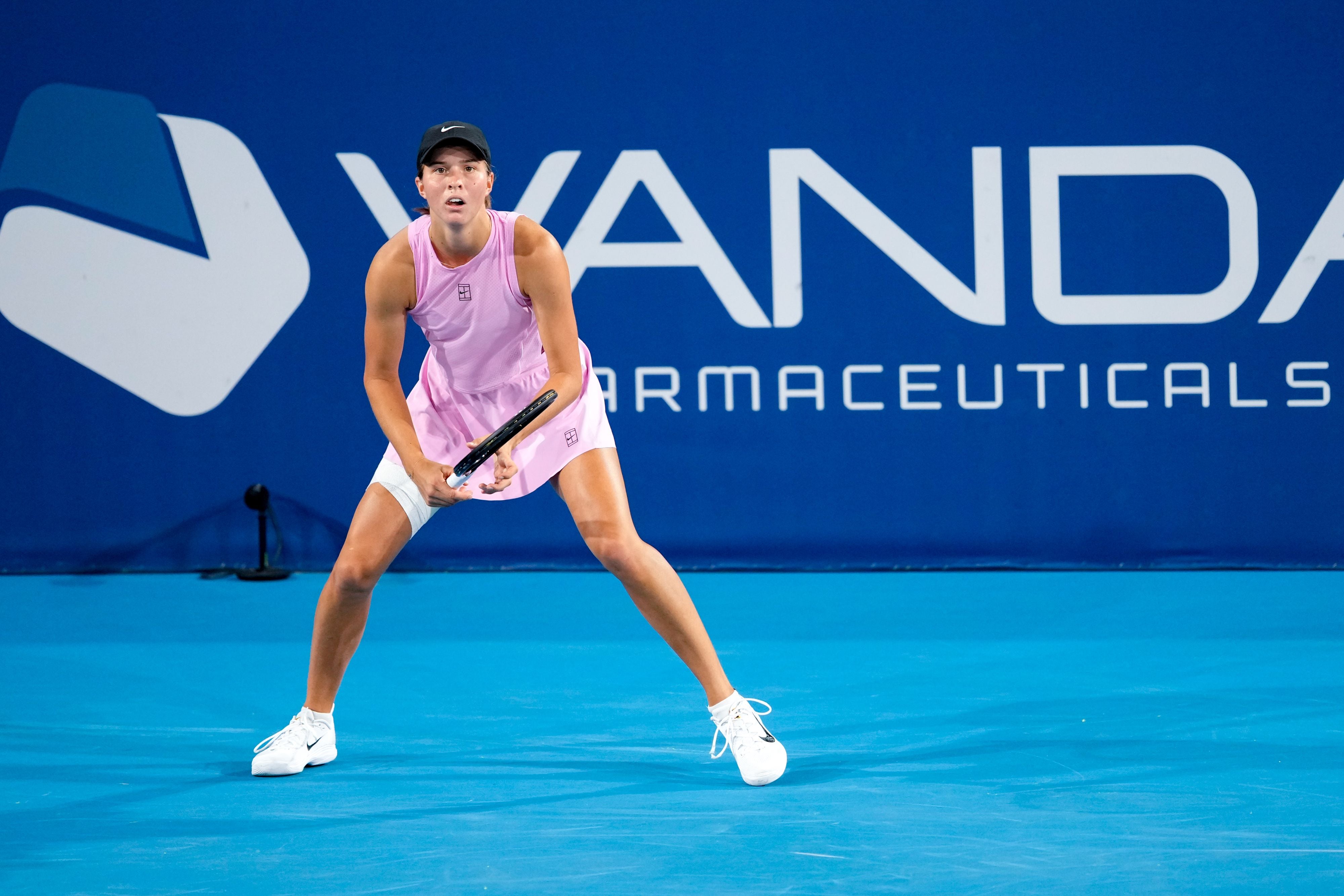 Tennisspielerin im rosa Kleid erwartet den Aufschlag bei einem Turnier auf blauem Platz.