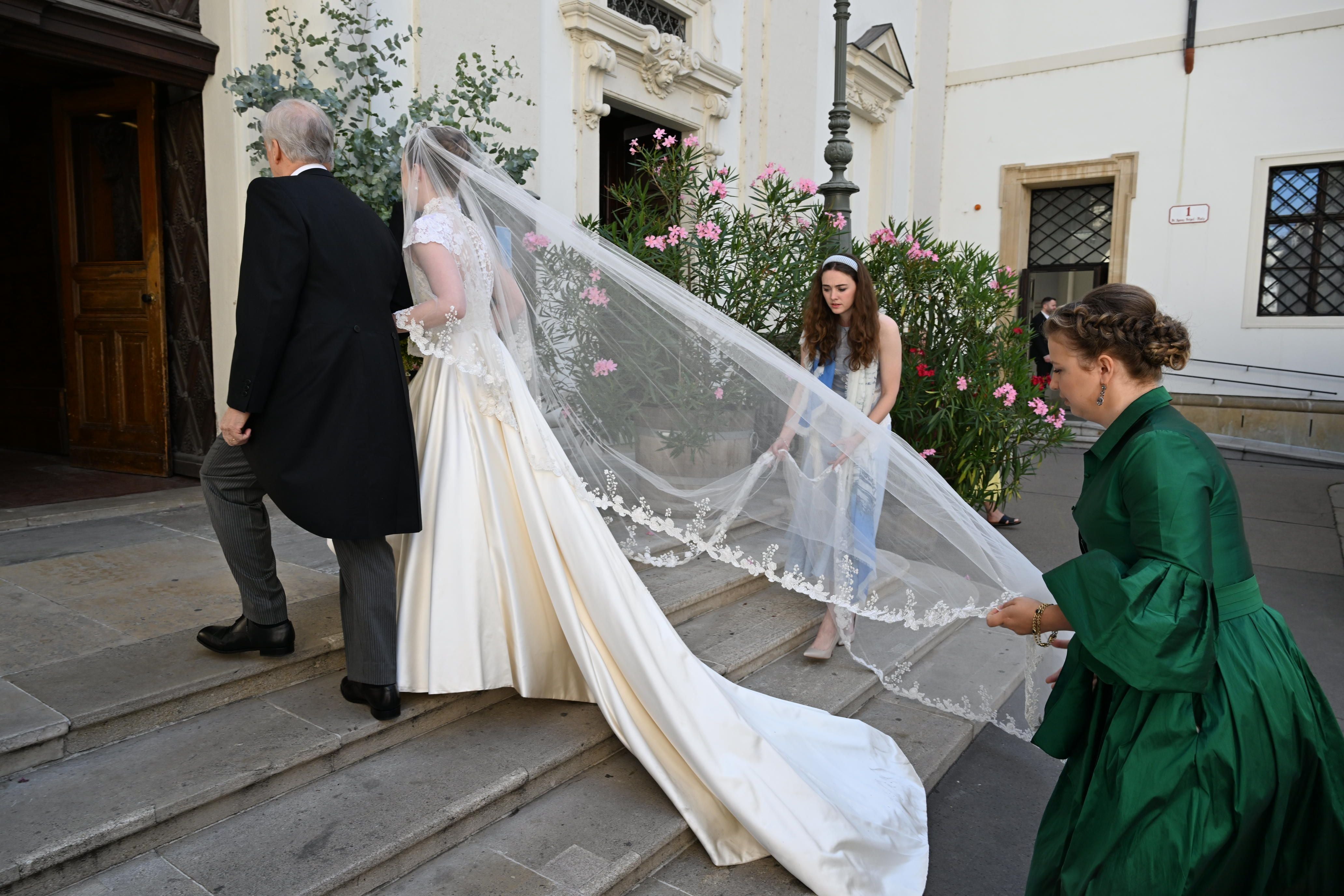 Braut im langen weißen Kleid mit Schleier betritt mit Begleitern eine Kirche bei einer Hochzeit.