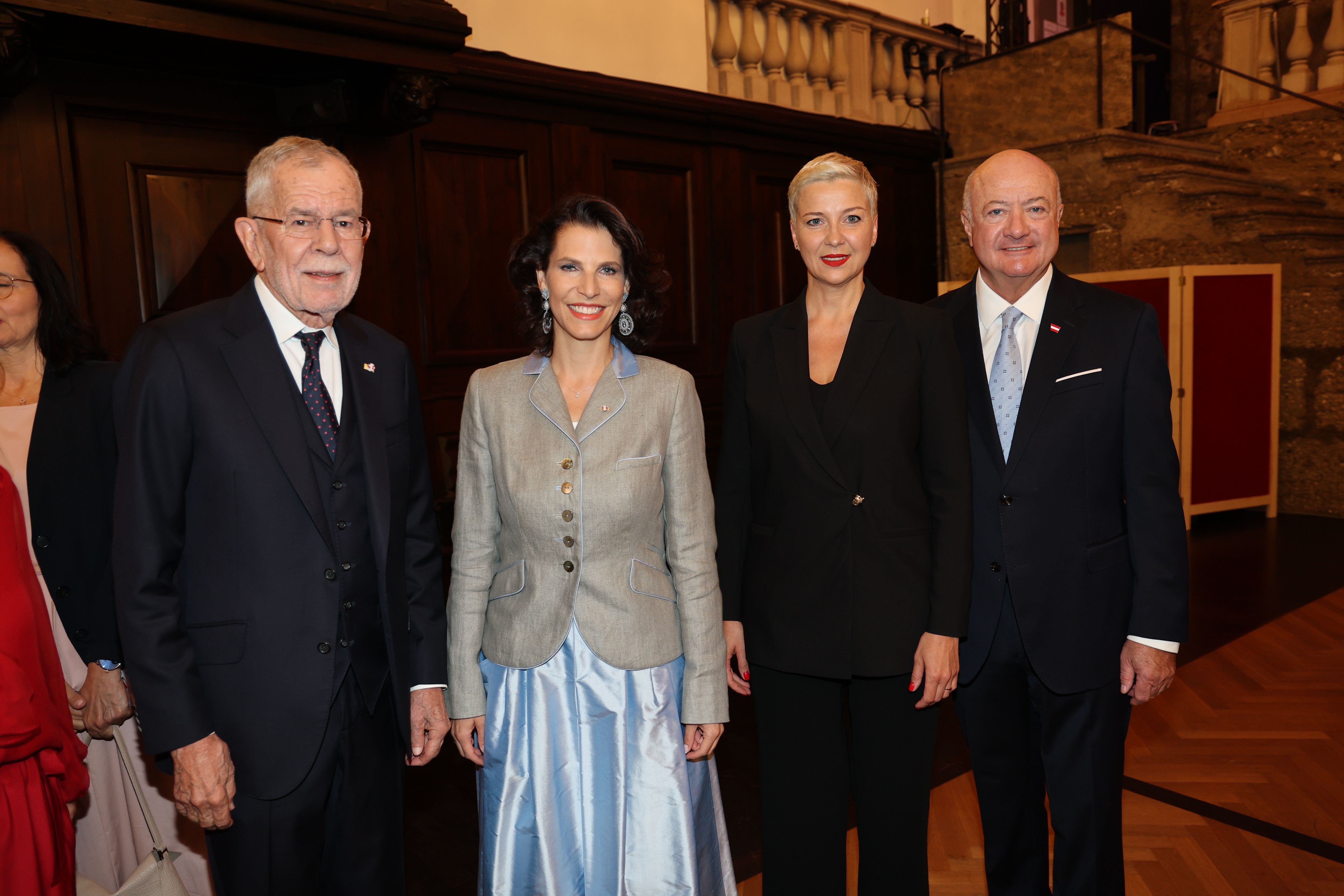 Vier elegant gekleidete Personen stehen nebeneinander bei einer Veranstaltung in einem Saal.