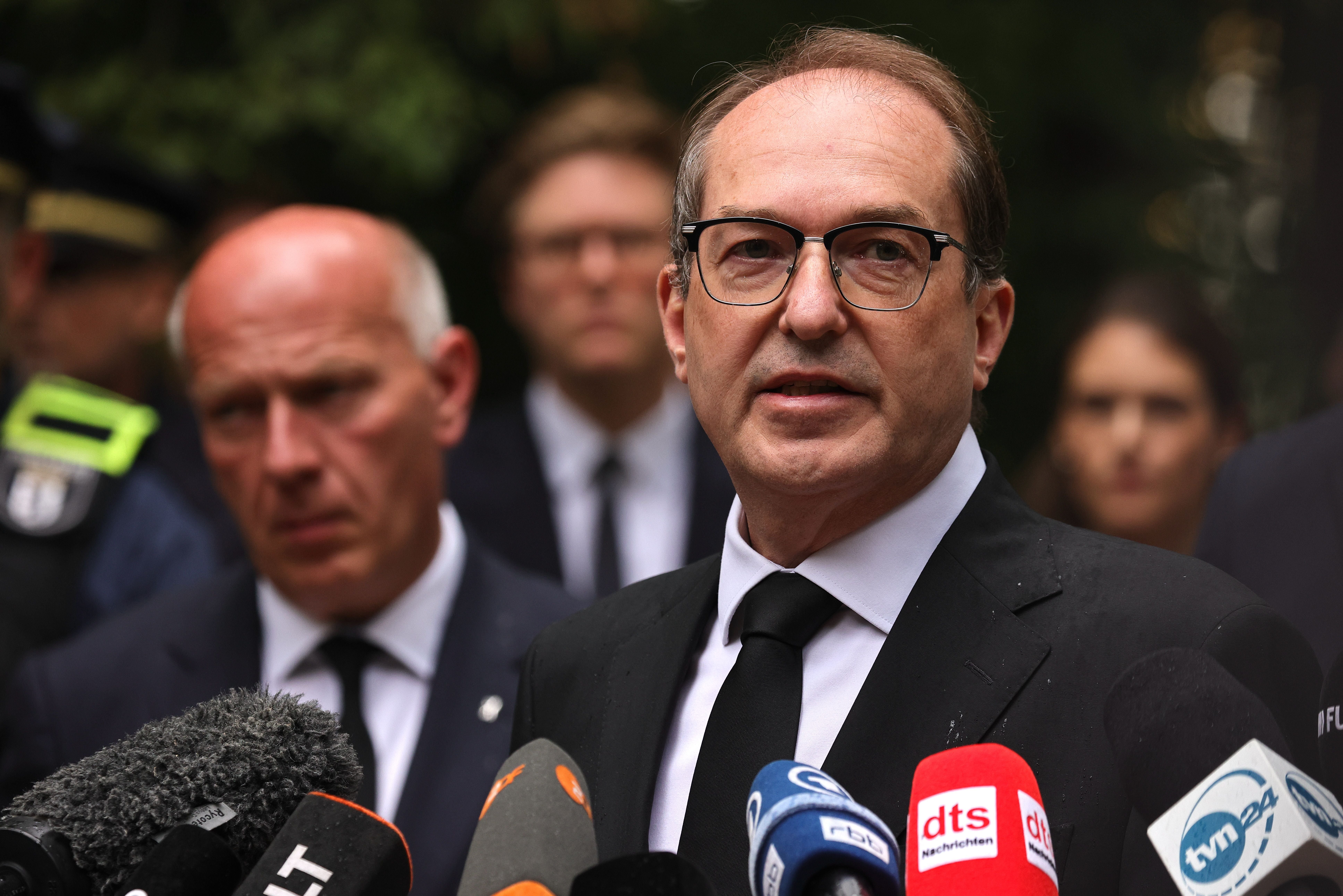 Ein Mann im Anzug spricht vor Mikrofonen bei einer Pressekonferenz im Freien.