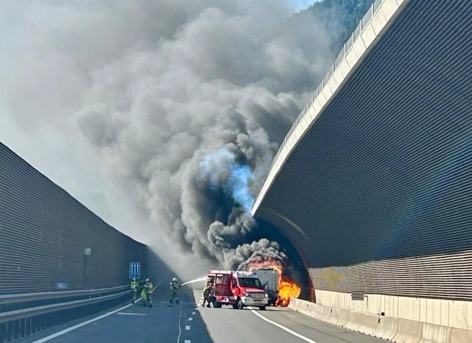 Ein brennendes Fahrzeug im Tunnel, dichter schwarzer Rauch, Feuerwehrleute im Einsatz.
