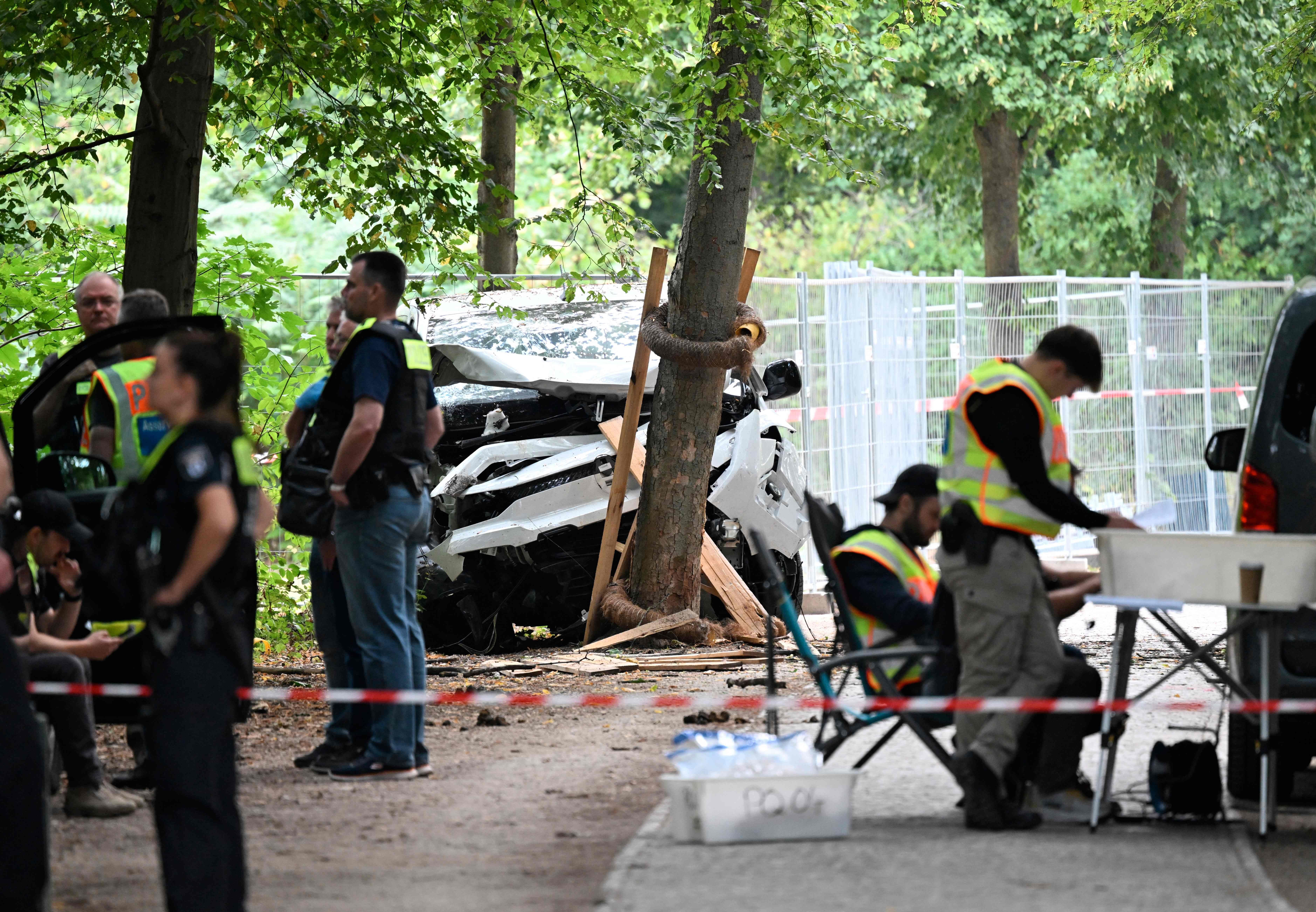 Polizeibeamte sichern einen Unfallort im Wald, ein weißes Auto ist gegen einen Baum geprallt.