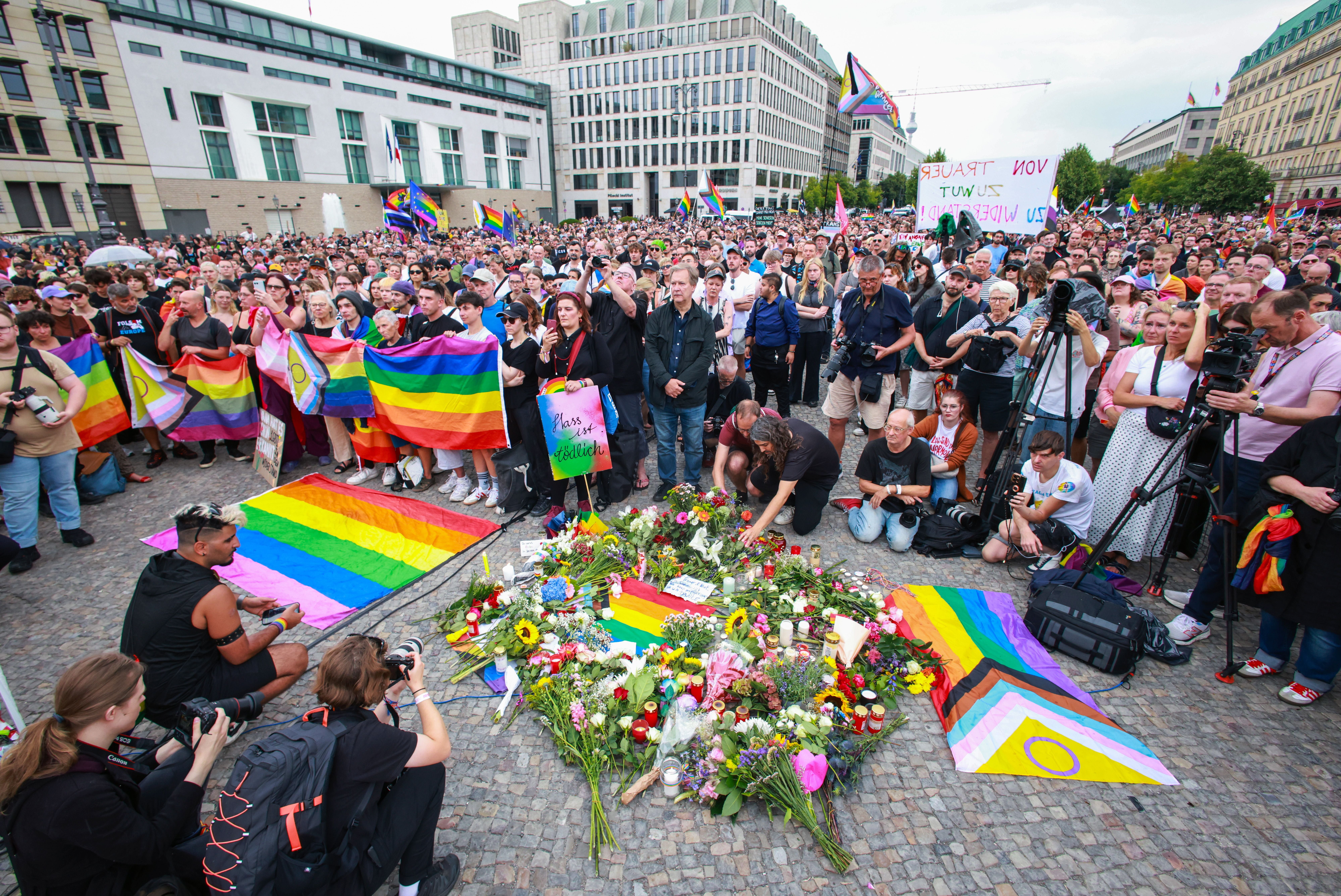 Menschen trauern mit Regenbogenflaggen und Blumen vor dem Brandenburger Tor in Berlin.
