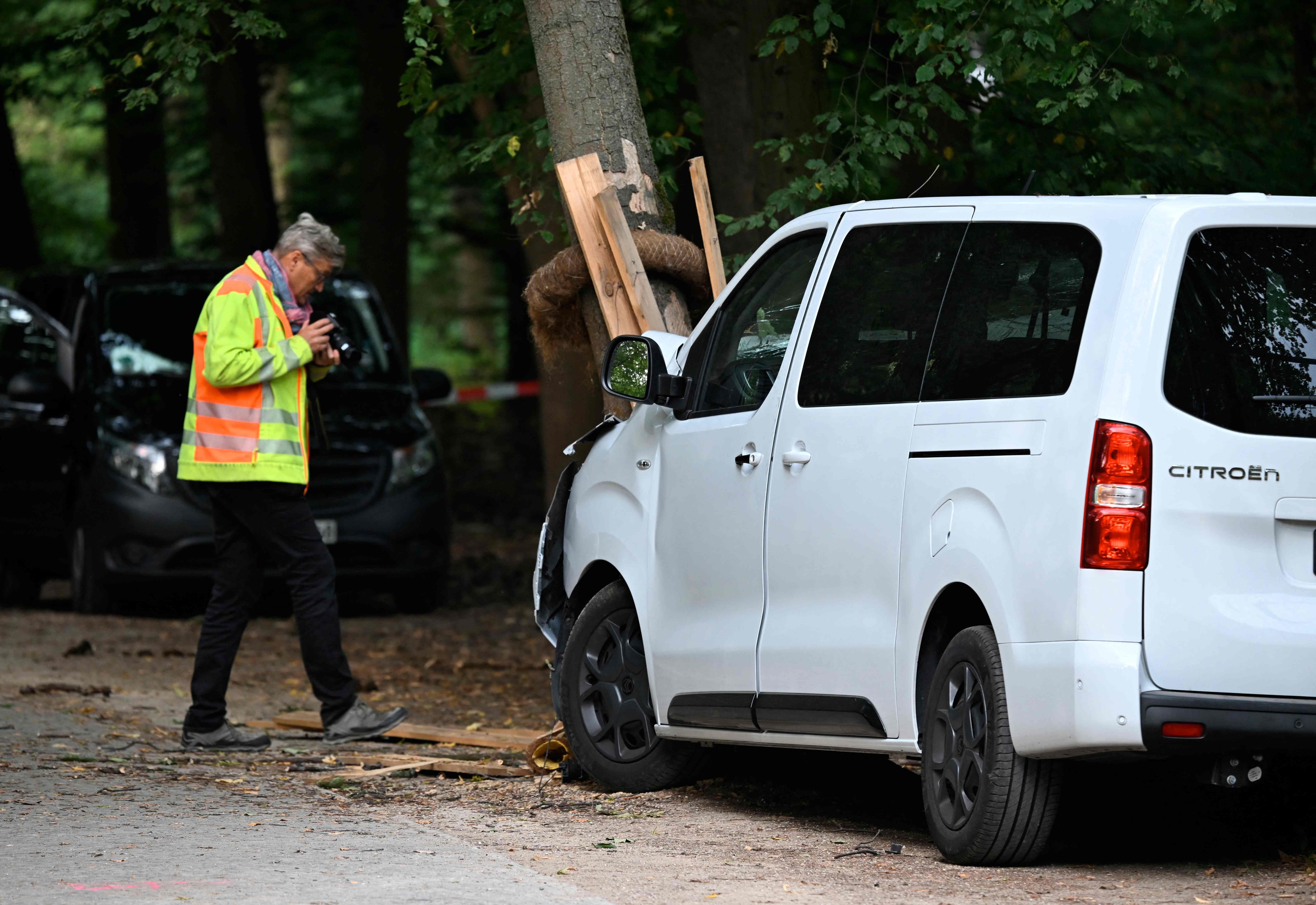 Ein weißer Citroën-Van ist frontal gegen einen Baum geprallt, daneben steht ein Ermittler mit Kamera.