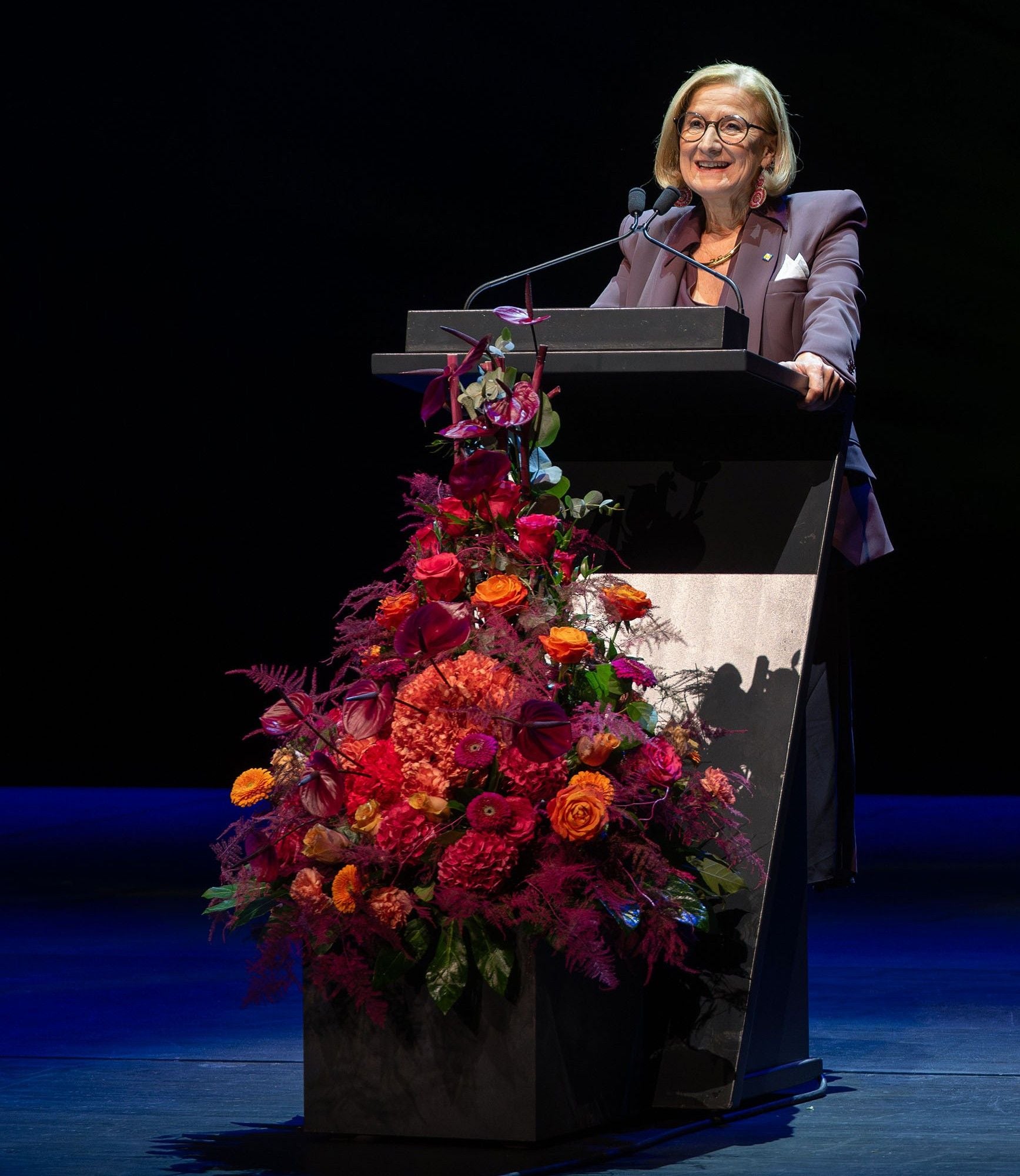 Frau am Rednerpult mit großem Blumenarrangement im Festspielhaus St. Pölten.