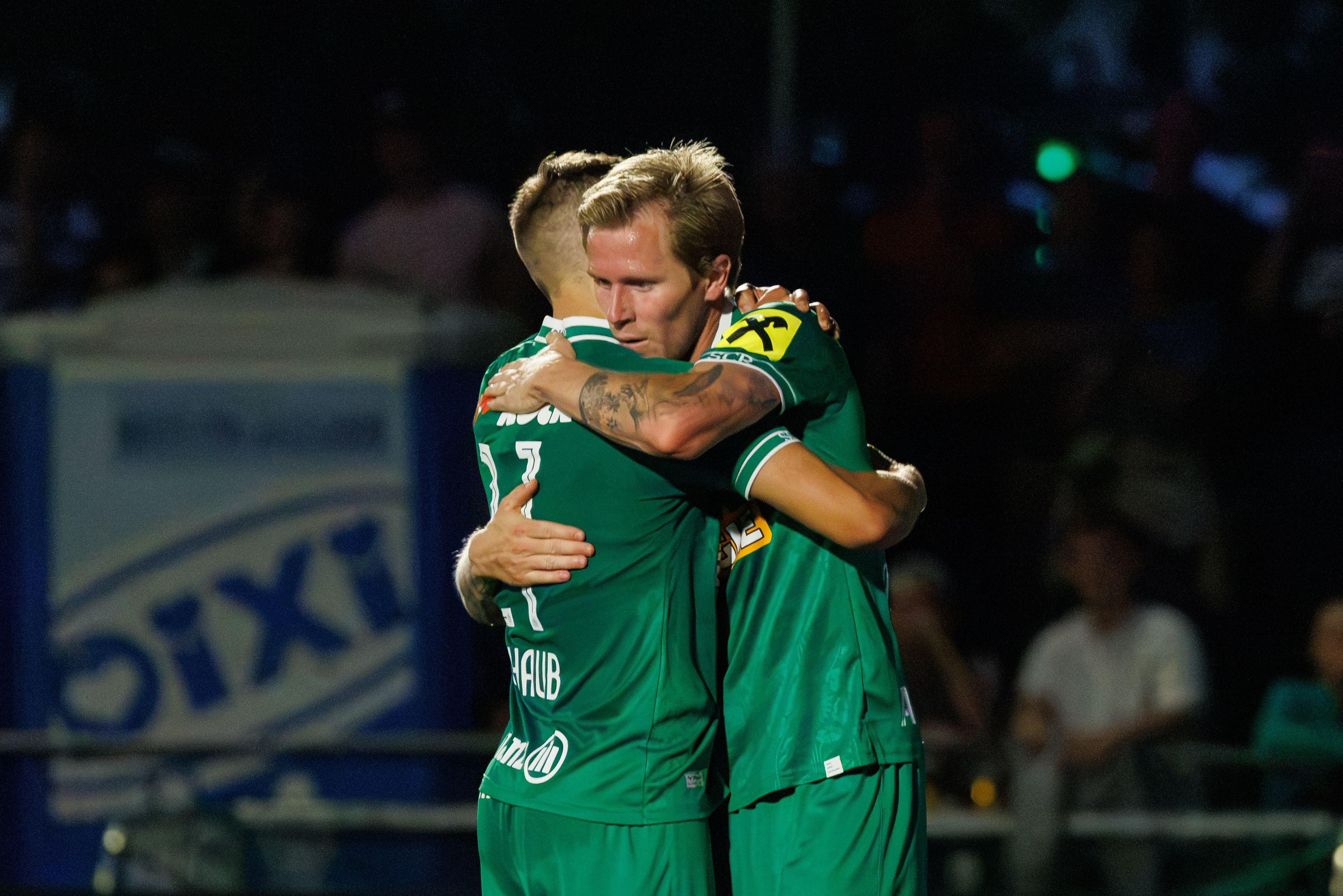 Zwei Rapid-Spieler umarmen sich während eines Fußballspiels im Stadion.