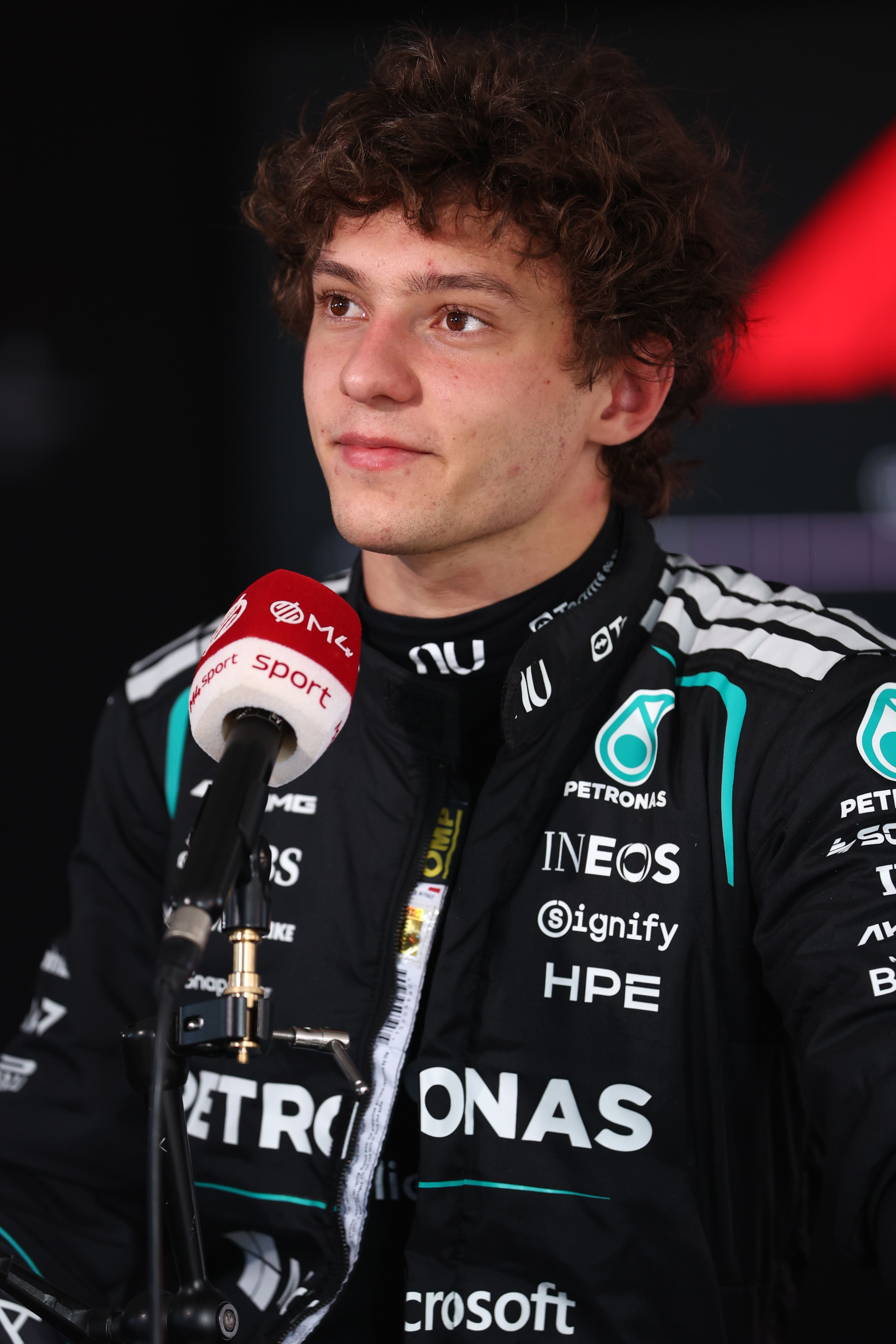 Ein junger Mann im Mercedes-Rennanzug spricht bei einem Interview in ein Mikrofon.