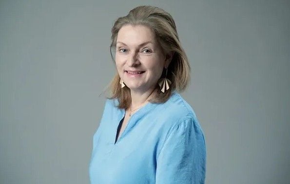 Frau mit hellblauer Bluse und auffälligen Ohrringen vor grauem Hintergrund.