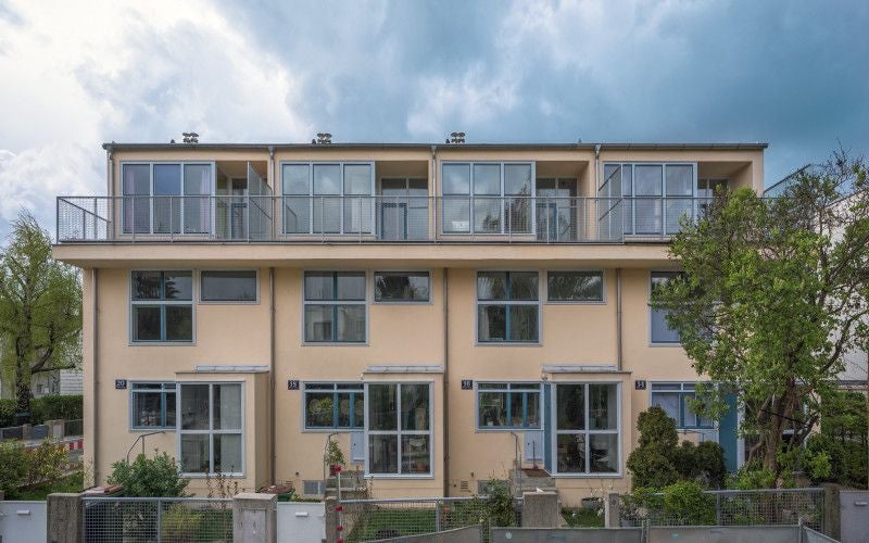 Modernisiertes Wohnhaus mit drei Etagen, großen Fenstern und Balkonen, umgeben von Bäumen.
