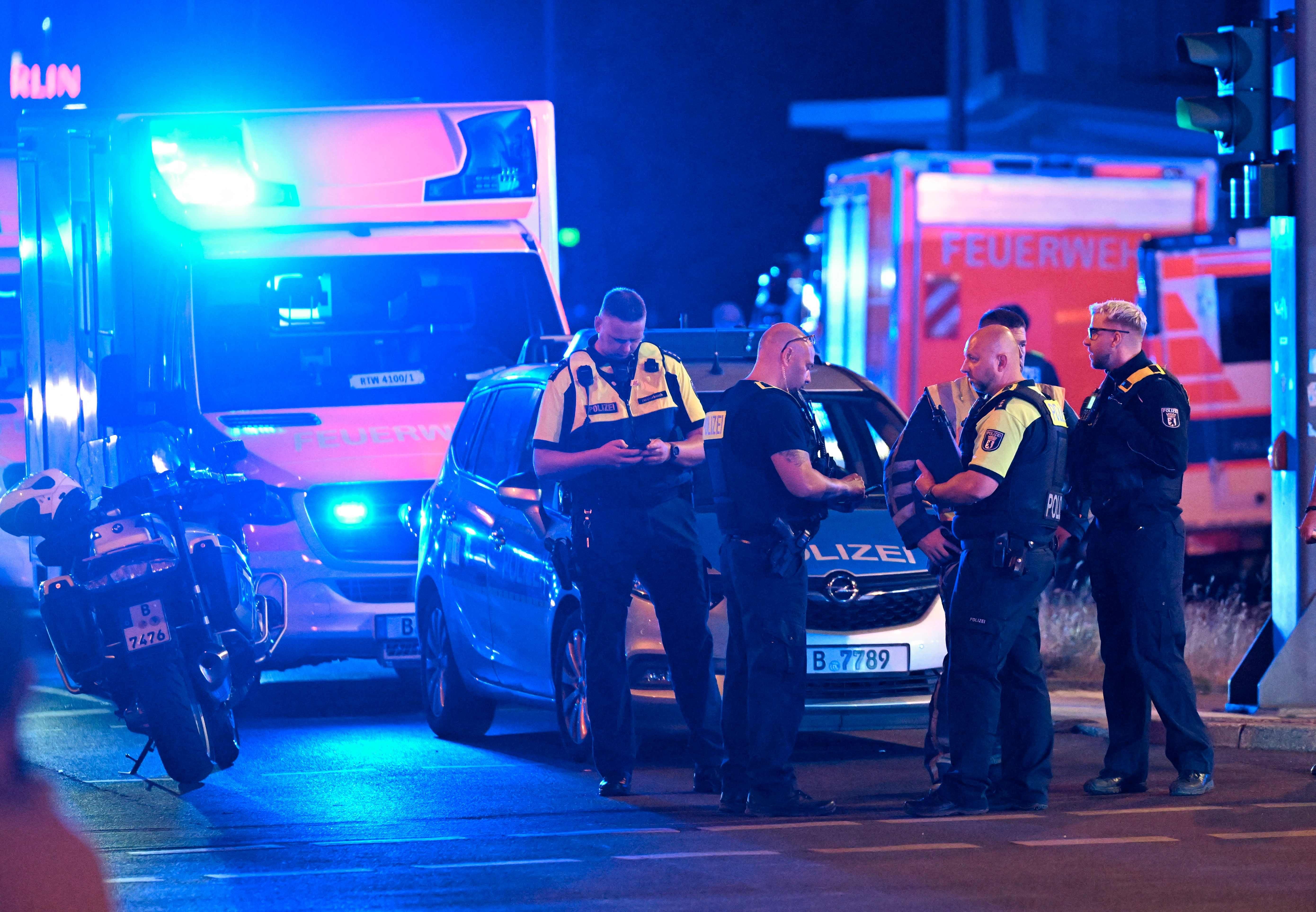 Mehrere Polizisten stehen nachts vor Einsatzfahrzeugen mit Blaulicht an einem Unfallort in Berlin.