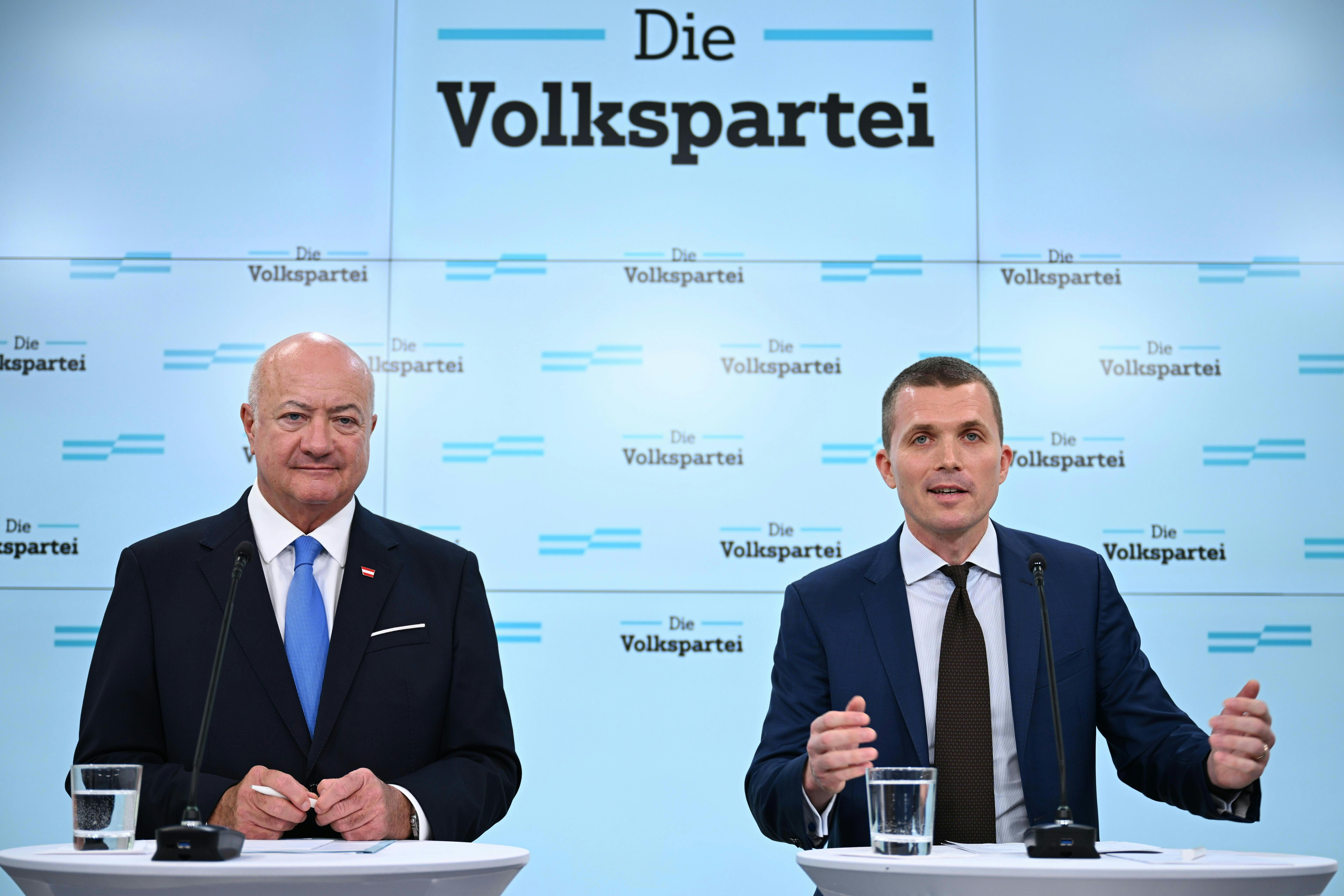 Zwei Männer im Anzug sprechen bei einer Pressekonferenz vor „Die Volkspartei“-Hintergrund.