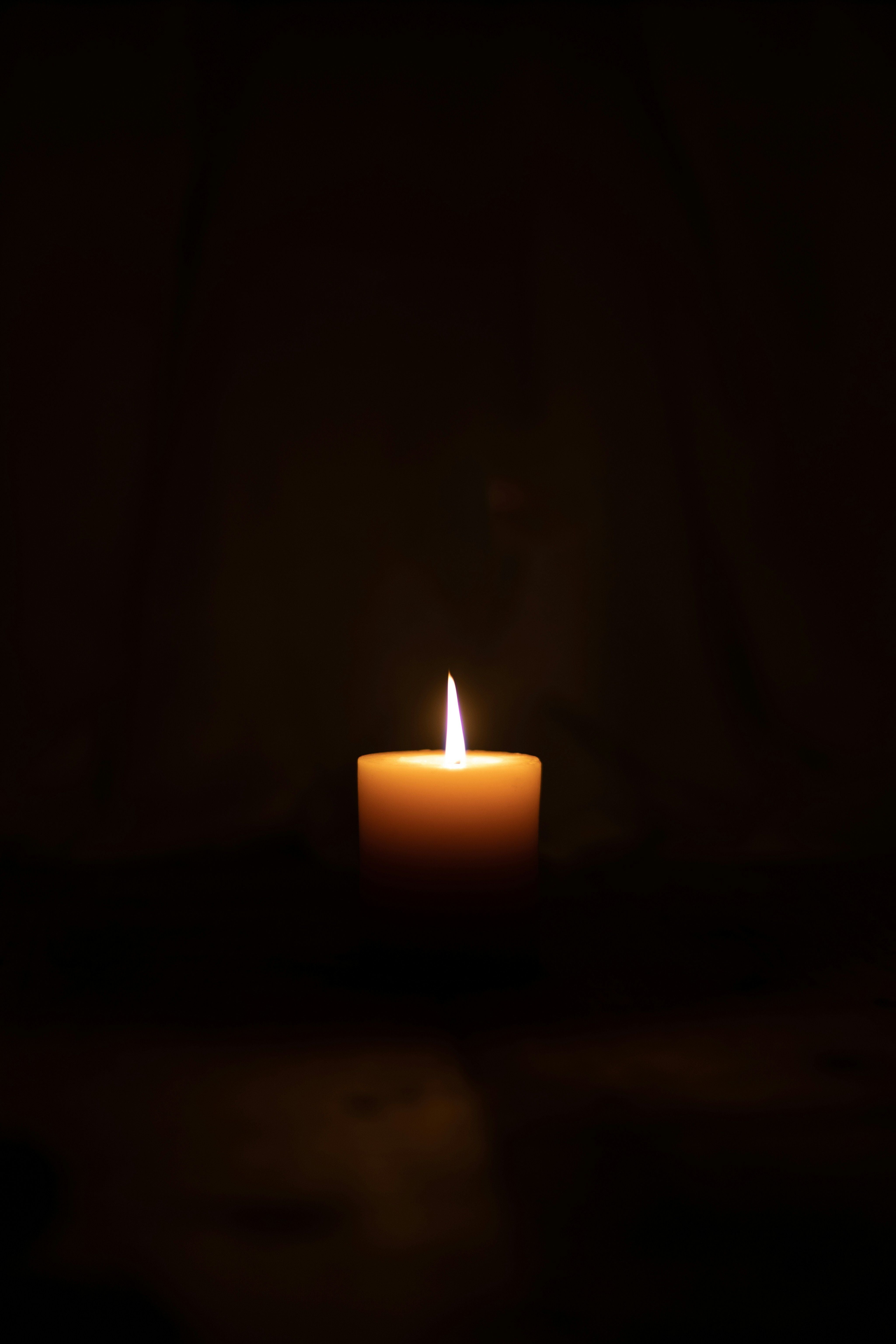 Eine brennende Kerze leuchtet in dunkler Umgebung.