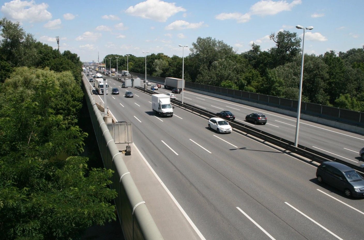 Autos und Lastwagen fahren auf der sechsspurigen, stark befahrenen A23 in Wien bei sonnigem Wetter.