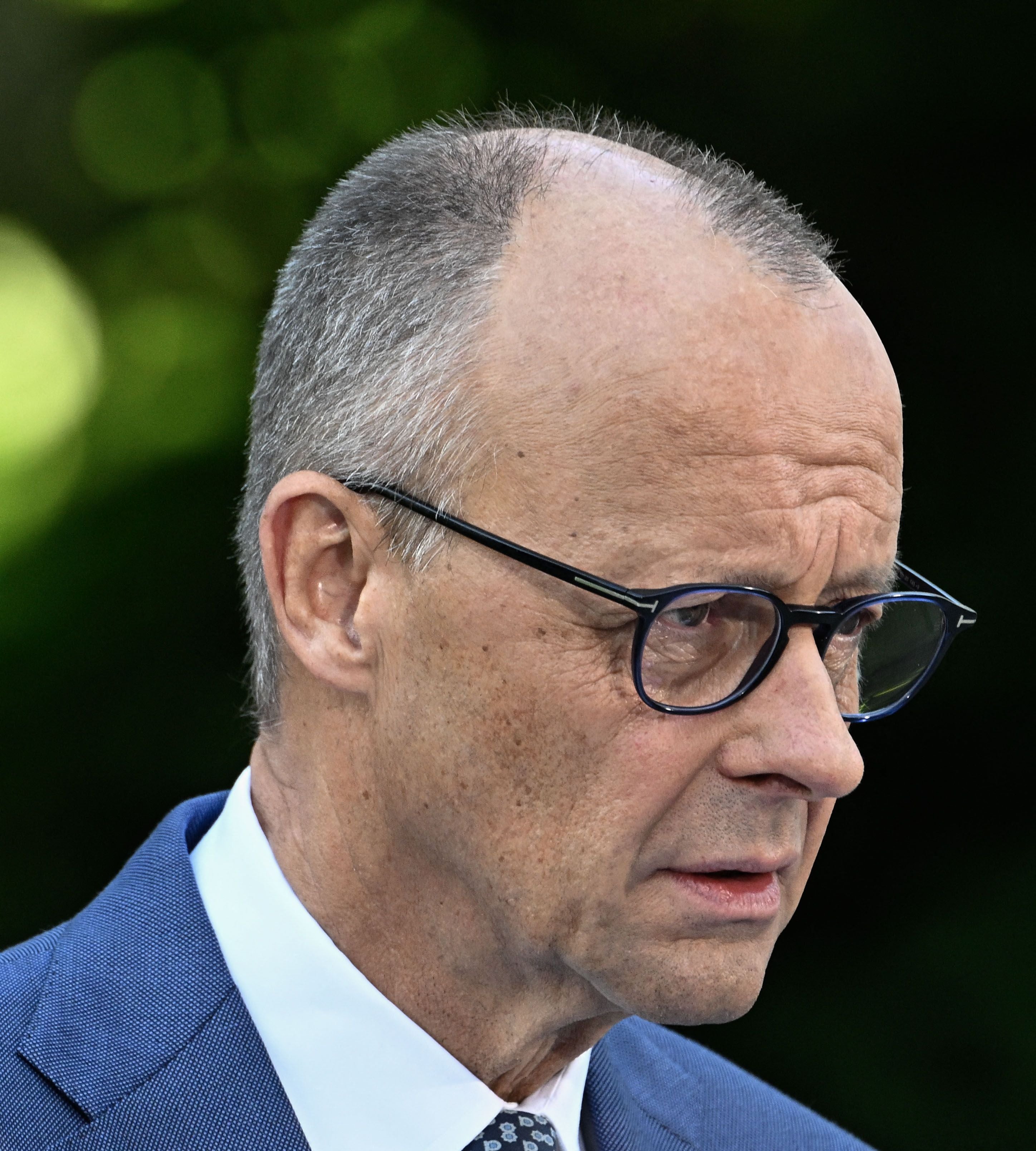 Ein älterer Mann mit Brille und Anzug spricht ernst im Freien.