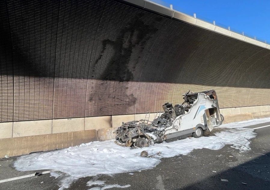 Ausgebranntes Wohnmobil an einer Tunnelwand, Löschschaum bedeckt den Boden.