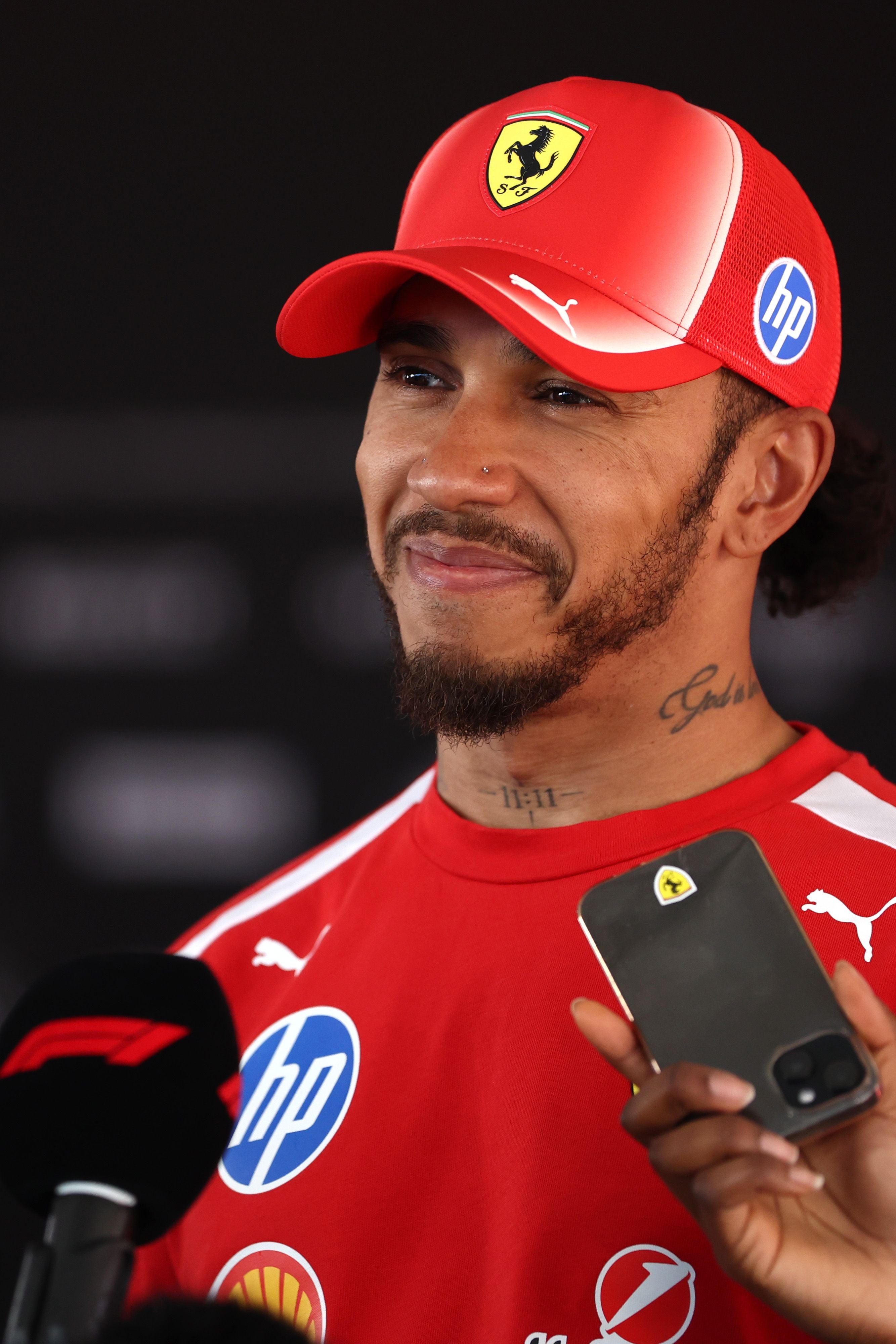 Lewis Hamilton im roten Ferrari-Outfit und Cap wird bei einem Interview befragt.