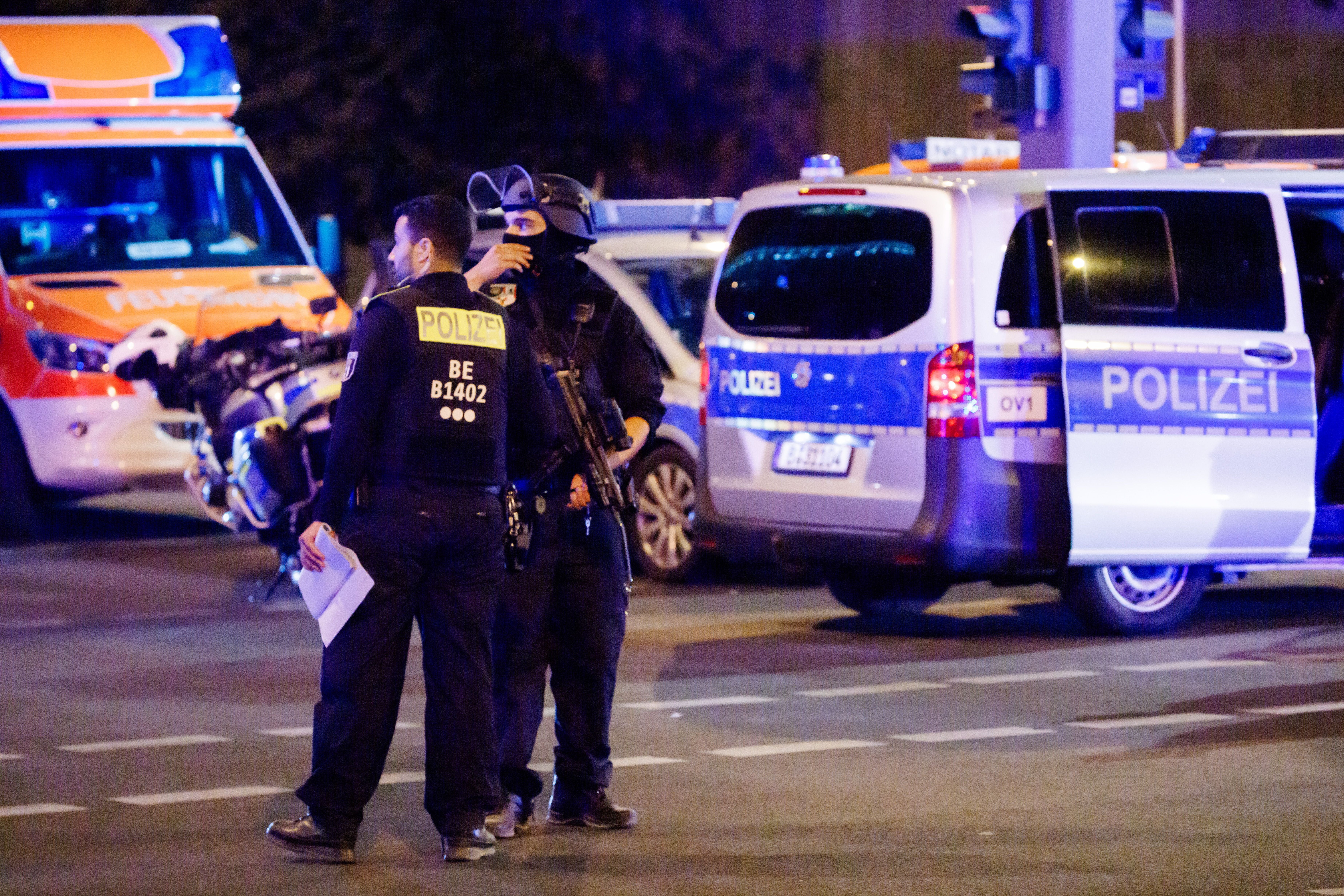 Zwei Polizisten an einem Einsatzort mit Polizei- und Rettungsfahrzeugen bei Nacht.