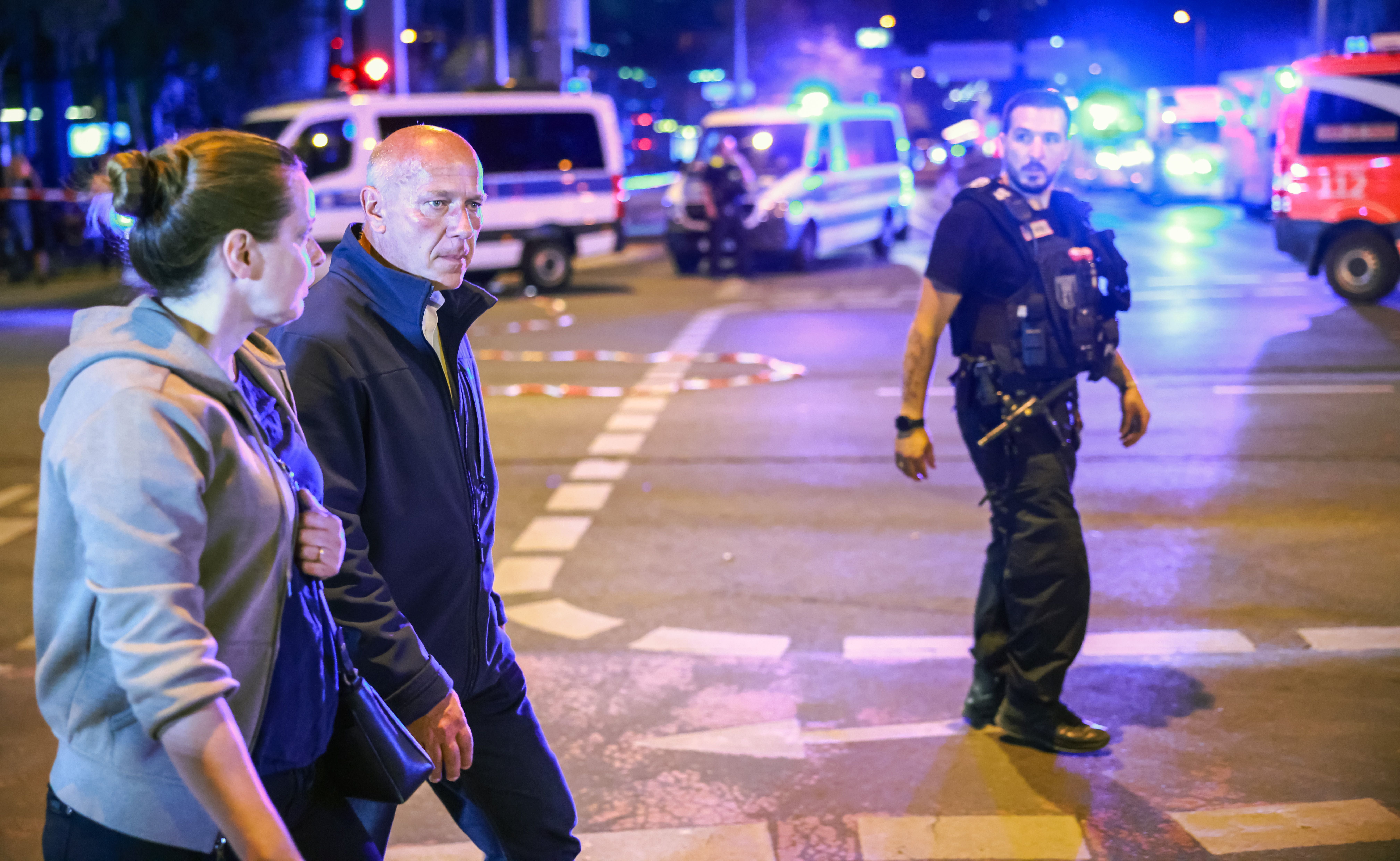 Ein Polizist und zwei Personen laufen nachts an einem abgesperrten Unfallort mit Blaulicht in Berlin vorbei.