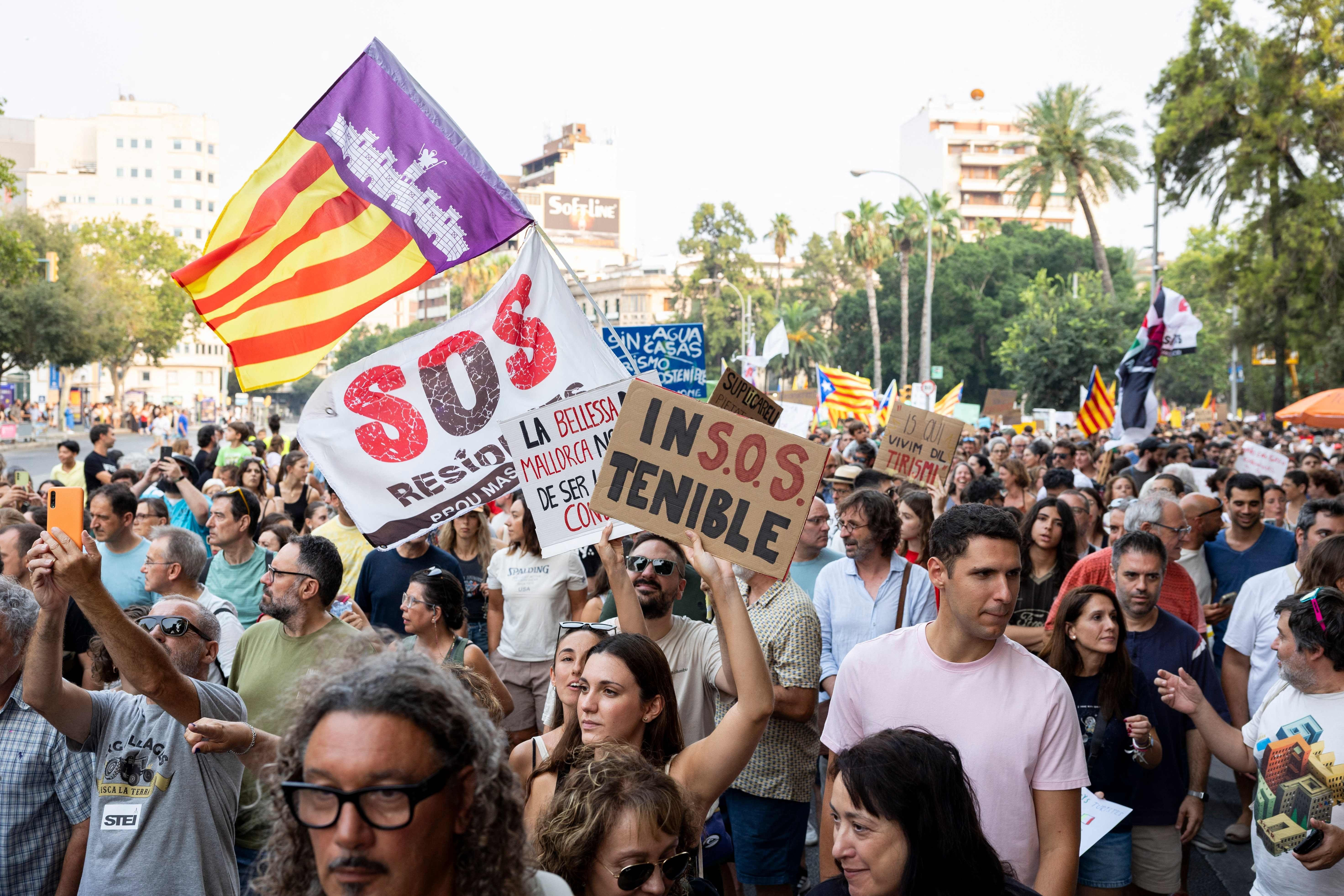 Menschen demonstrieren in Palma mit SOS-Plakaten gegen Overtourismus und hohe Wohnkosten.
