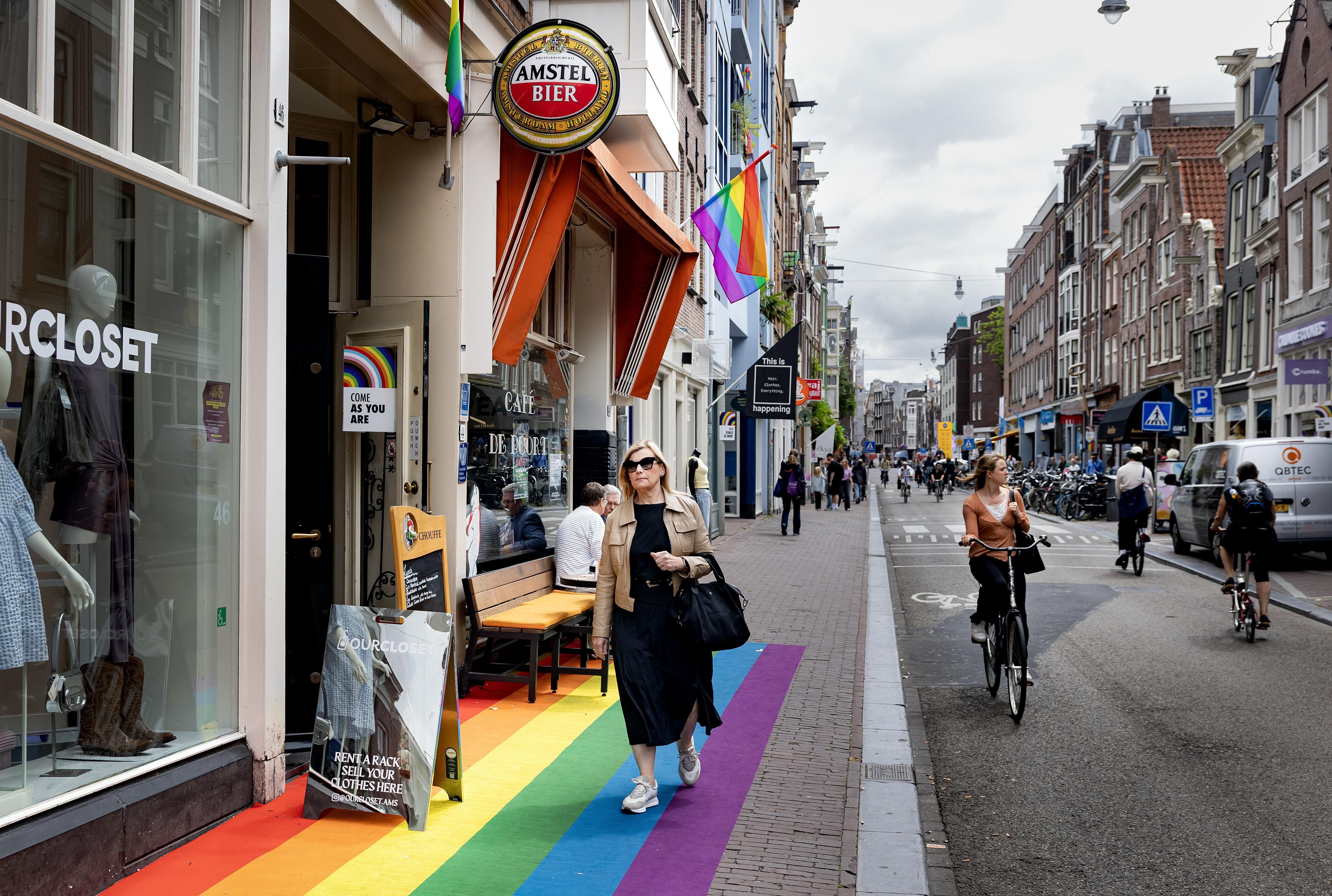 Menschen gehen und fahren Fahrrad auf einer mit Regenbogenfarben bemalten Straße in Amsterdam.