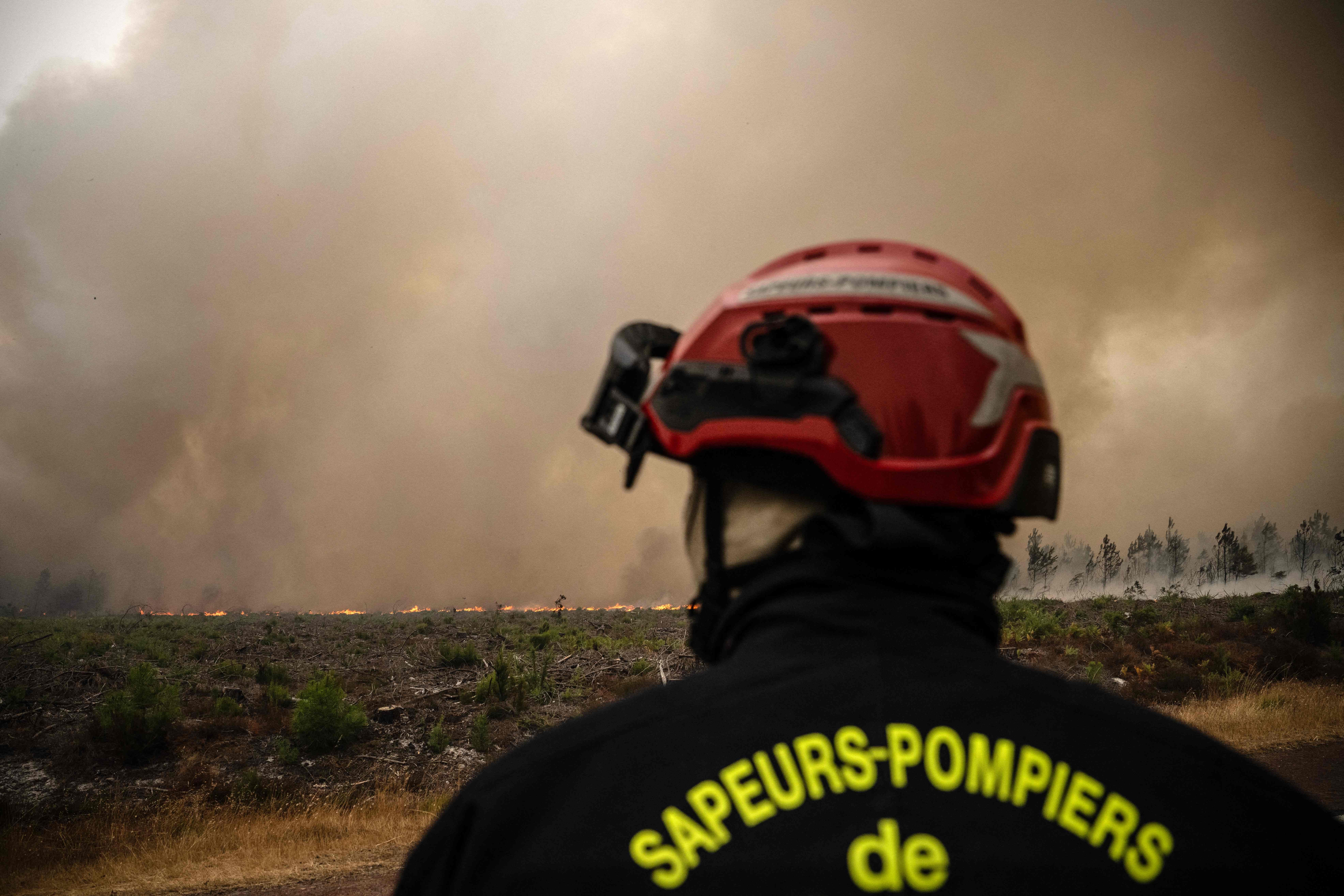 Ein Feuerwehrmann blickt auf einen brennenden Waldrand vor dichtem Rauch in Südwestfrankreich.