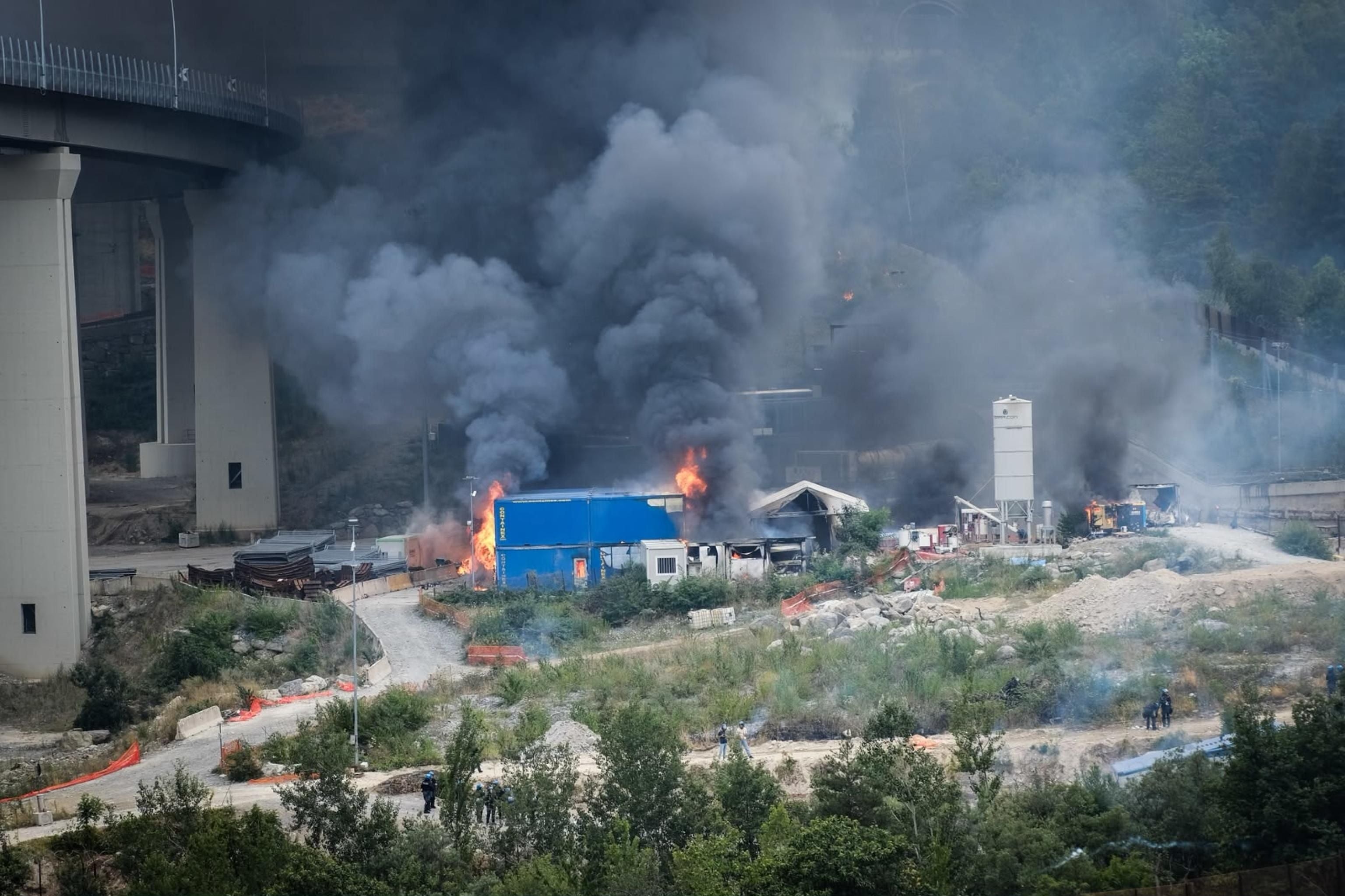 Dichter schwarzer Rauch steigt von brennenden Gebäuden auf einer Baustelle im Tal auf.