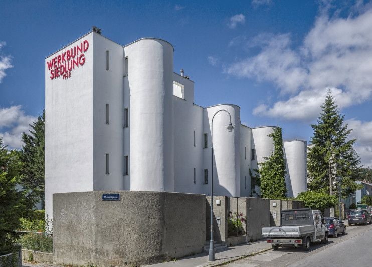 Modernes weißes Gebäude der Wiener Werkbundsiedlung mit Rundungen und rotem Schriftzug.