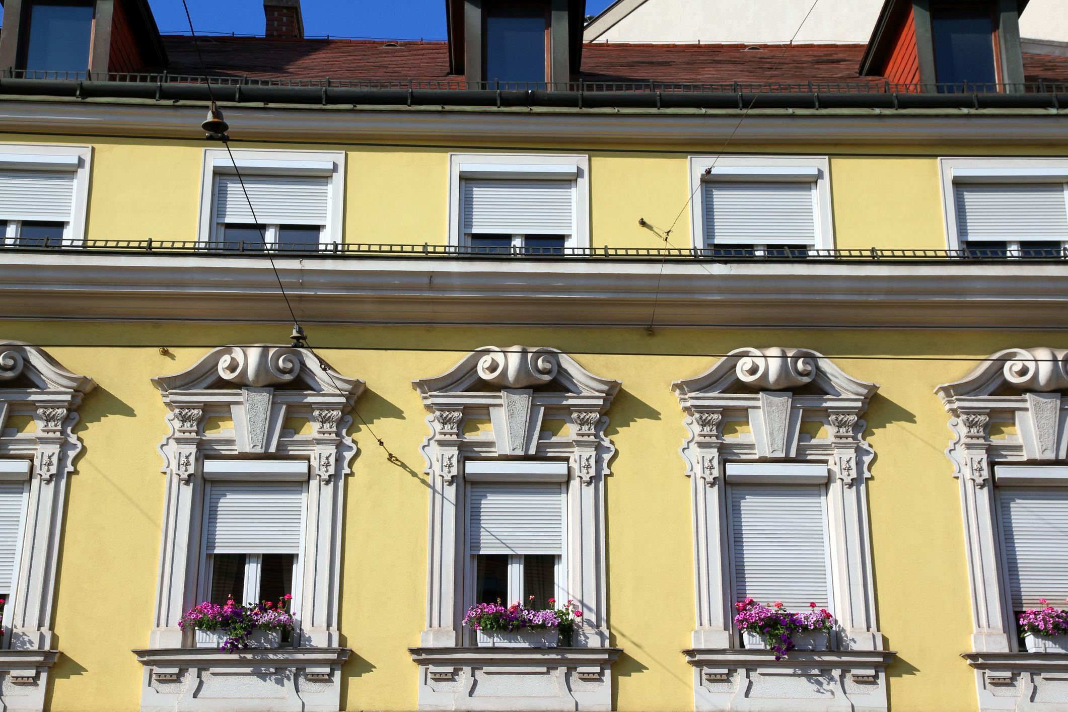 Gelbes Haus mit verzierten Fenstern, Blumenkästen und geschlossenen Rollläden in Wien.