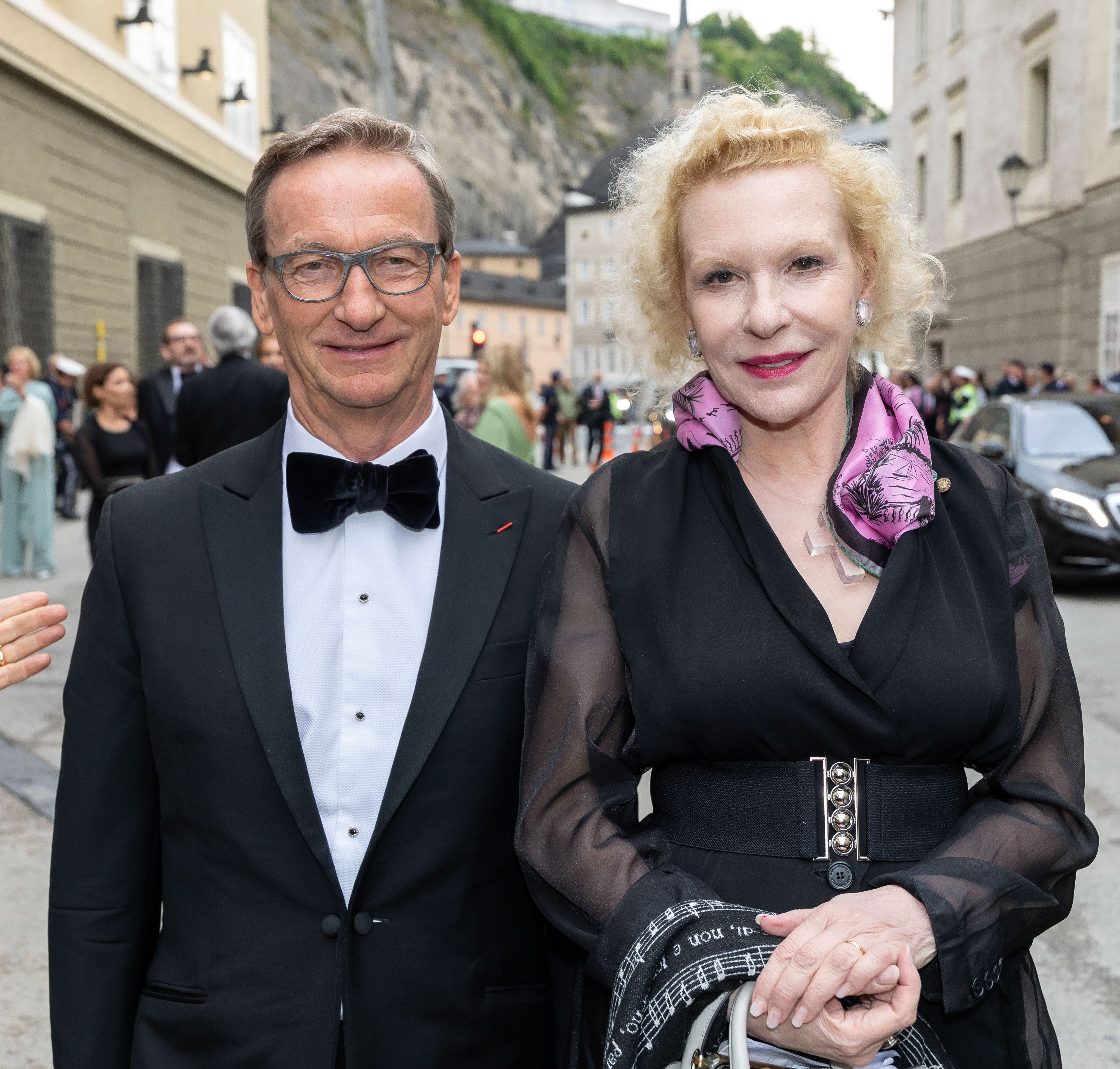 Ein elegant gekleidetes Paar steht lächelnd im Freien bei einer Festspielpremiere.