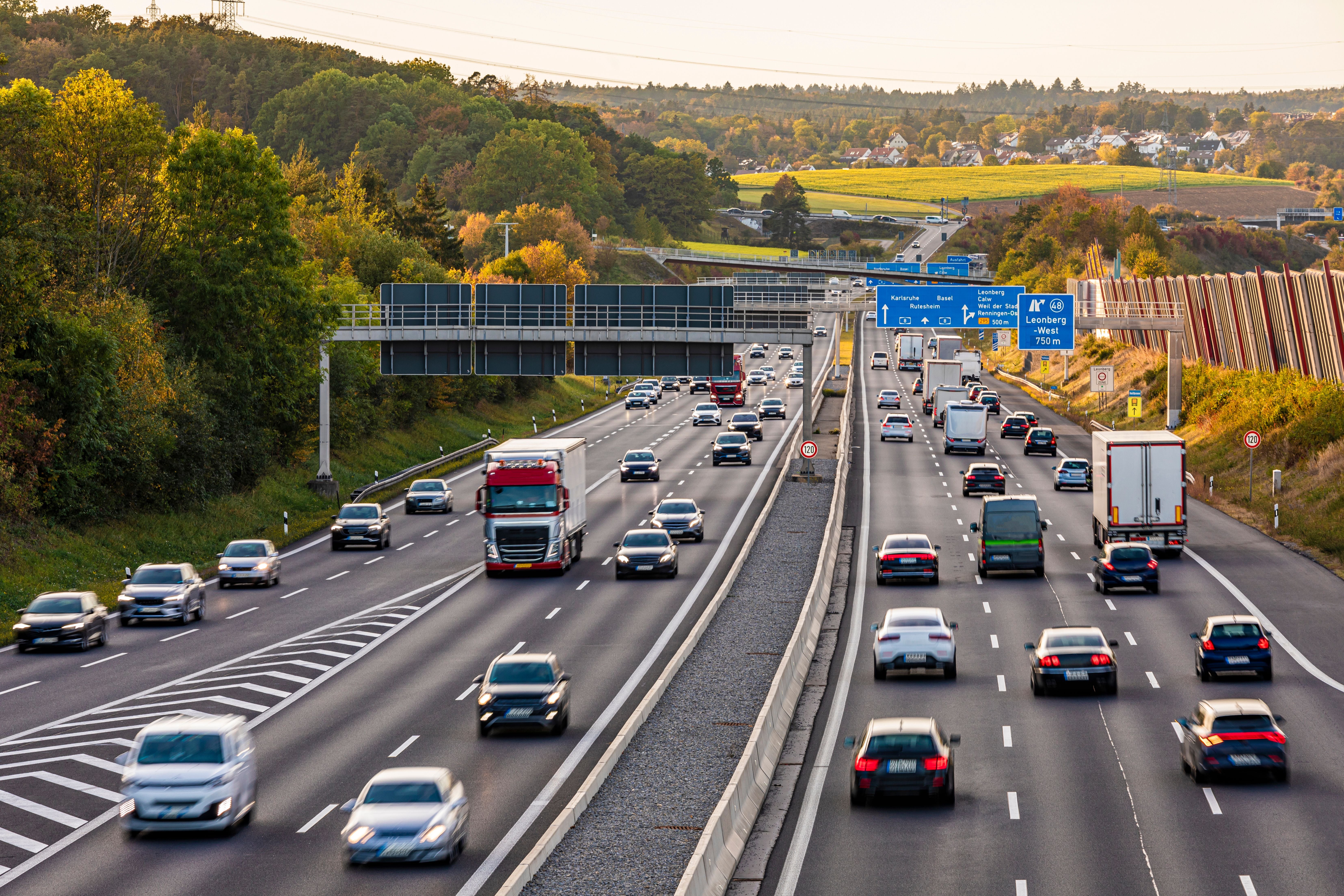 Viele Autos und LKWs fahren auf einer deutschen Autobahn bei Tageslicht, umgeben von Bäumen.