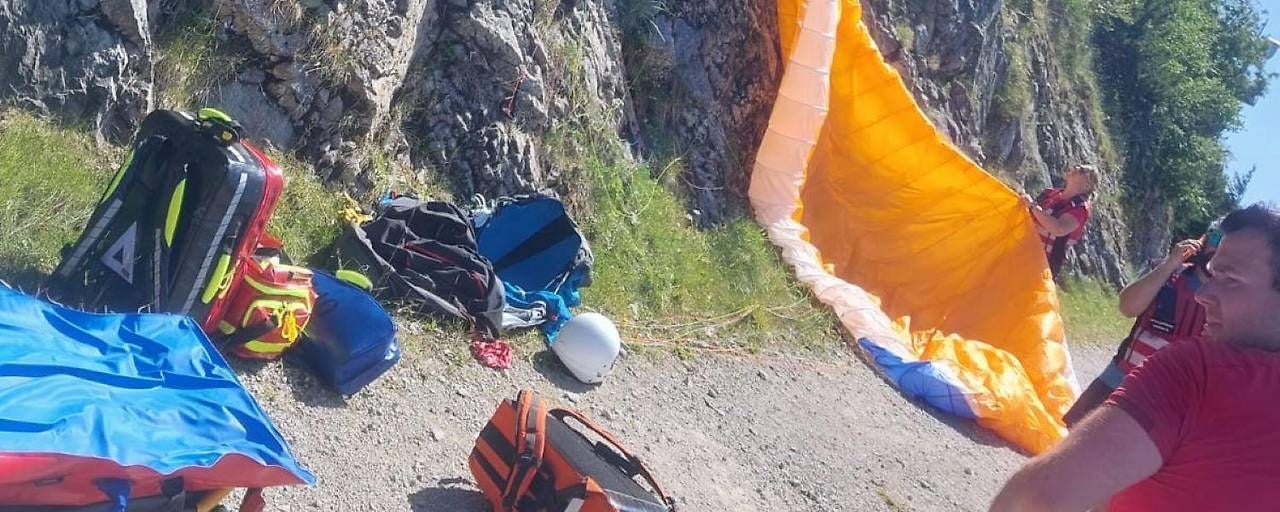 Rettungskräfte und Ausrüstung neben einem abgestürzten Gleitschirm an einem steinigen Hang.