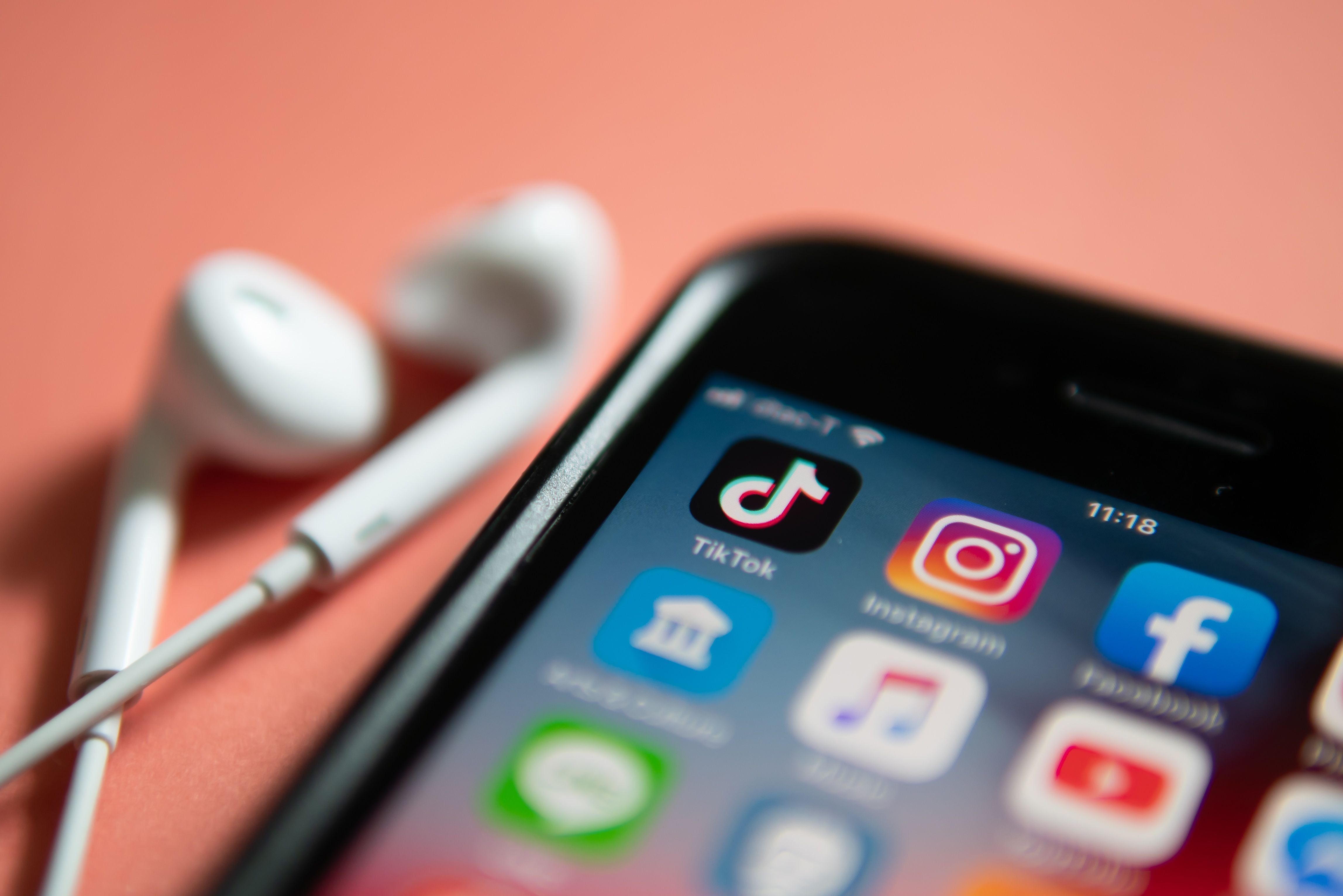 Nahaufnahme von Ohrhörern neben einem iPhone mit Social-Media-Apps wie TikTok, Instagram und Facebook.
